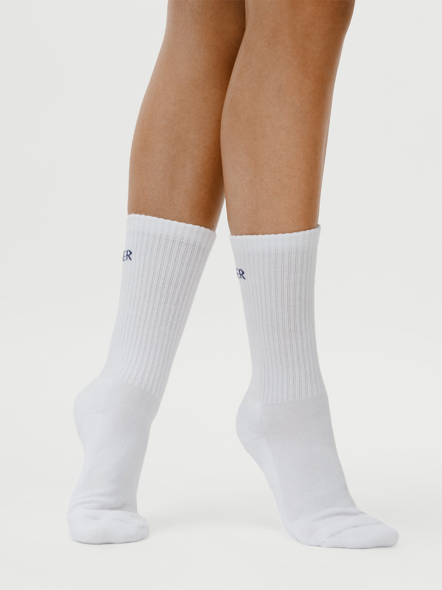 Eine Person, die auf Zehenspitzen steht, trägt LeGer x Oh April - Sue Socks Stronger (Größe 36) von LeGer by Lena Gercke, einfarbig weiße, gerippte Socken, vor einem weißen Hintergrund. Größe des Modells: 1,73 m.