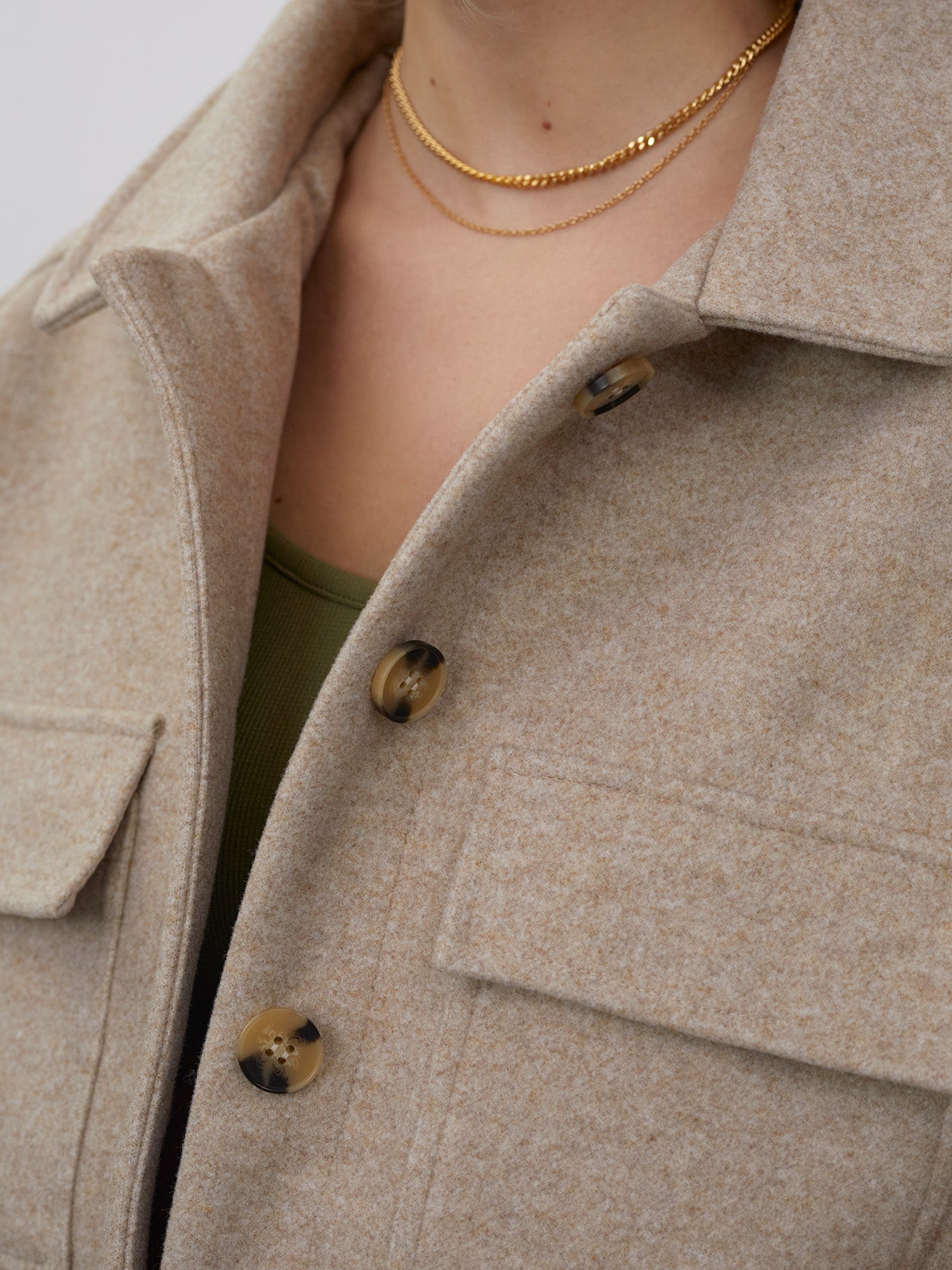Eine Nahaufnahme zeigt eine Person, die die beige Wolljacke „Eva“ von LeGer by Lena Gercke mit großen Knöpfen über einem grünen Oberteil trägt. Sie trägt zwei zarte goldene Halsketten. Der Mantel hat eine normale Länge, wobei die Textur und die Knopfdetails betont werden.