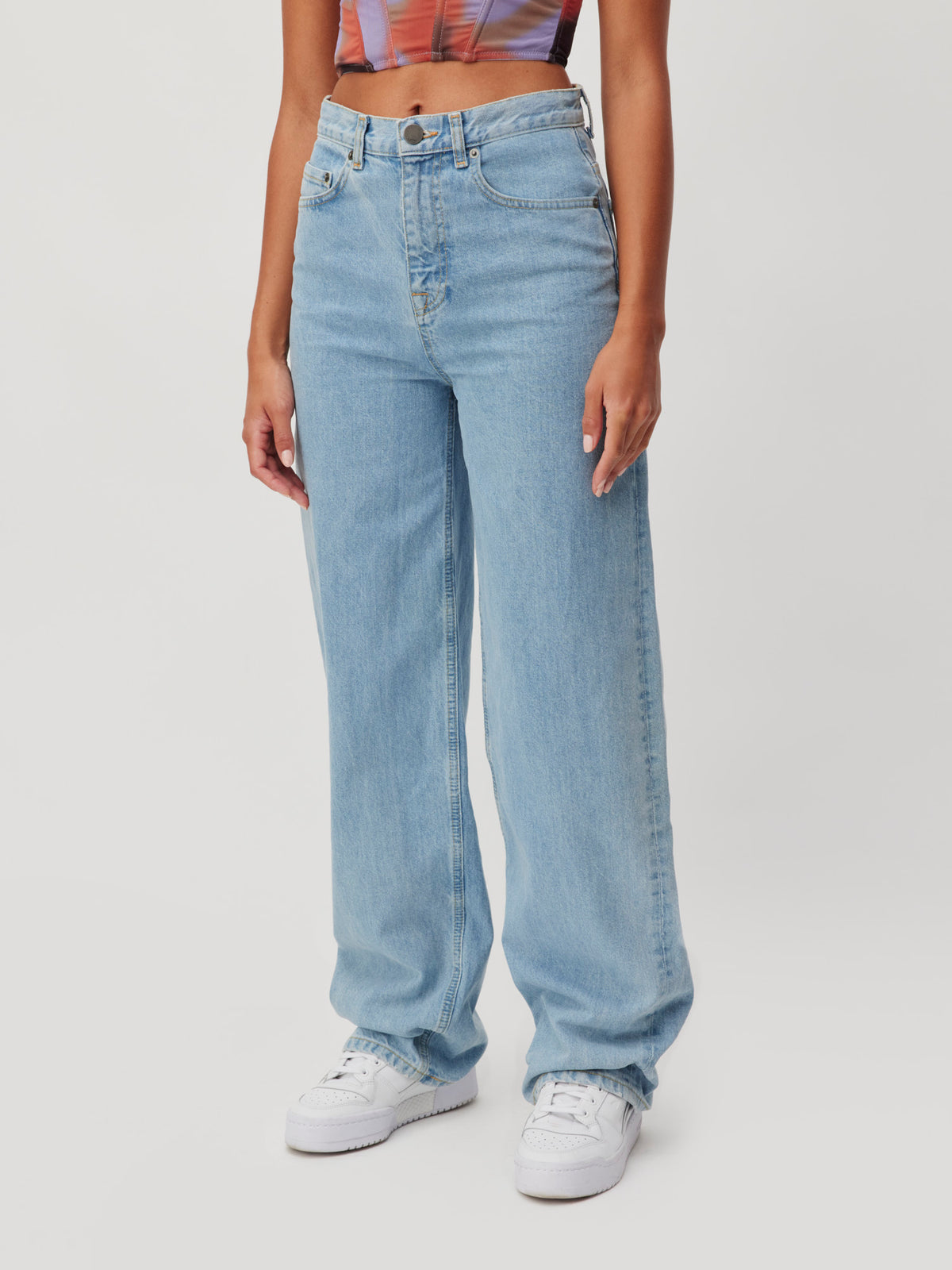Eine Person, die eine hellblaue, hoch taillierte LeGer by Lena Gercke „Carla“-Hose mit weitem Bein und weiße Sneaker trägt.