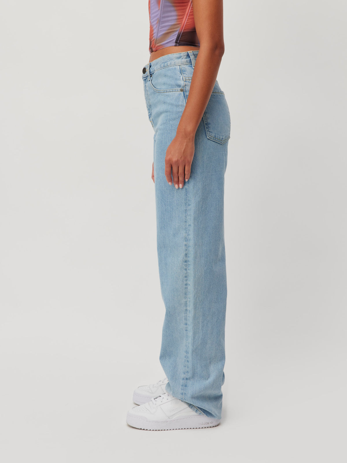 Seitenansicht von Lena Gercke in einer blauen Jeanshose „Carla“, kombiniert mit einem bunten bauchfreien Top und weißen Sneakers.