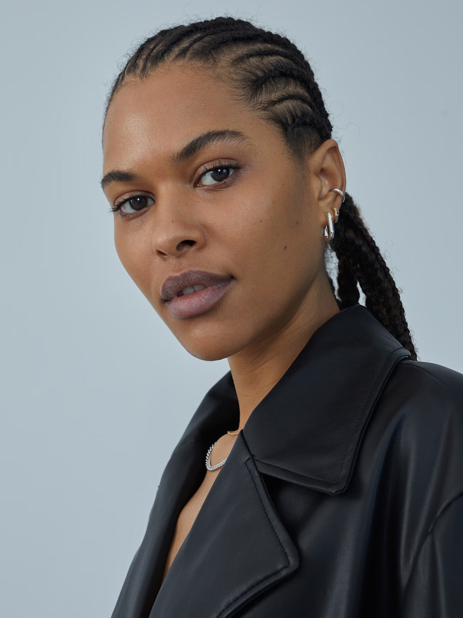 Eine Person mit eng geflochtenen Haaren, silbernen Creolen und der Marla-Jacke von LeGer by Lena Gercke blickt vor einem hellblauen Hintergrund in die Kamera und präsentiert die perfekt sitzende Kleidung.