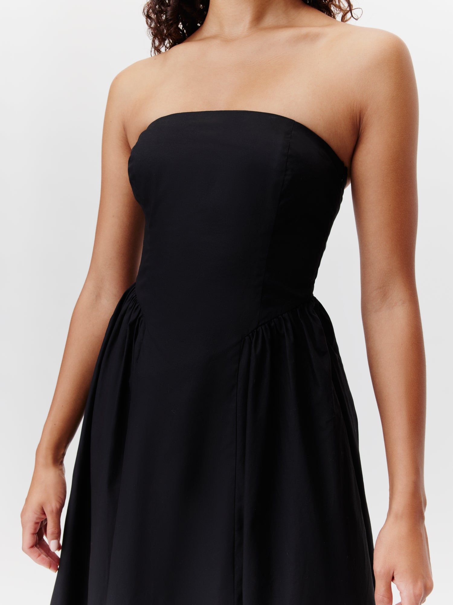 Eine Frau präsentiert das „Vianne“-Kleid von LeGer by Lena Gercke – ein schwarzes, trägerloses 7/8-Kleid mit figurbetontem Schnitt und schwingendem Rock – vor weißem Hintergrund. Ihr Gesicht bleibt verborgen.