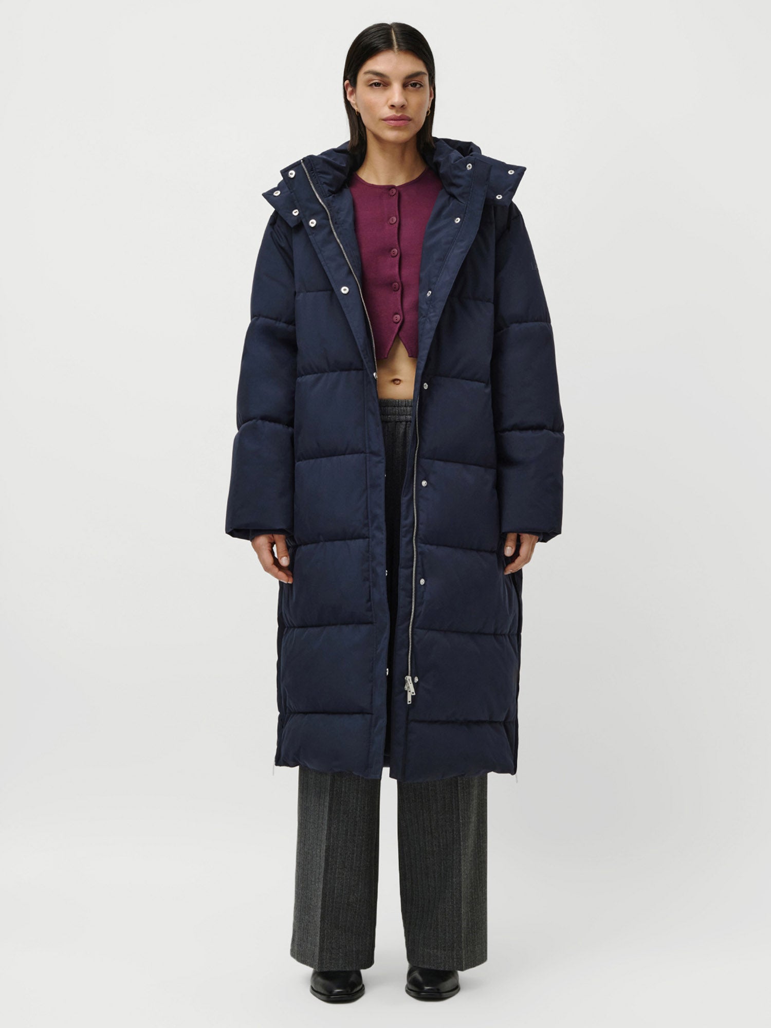 Eine Person steht mit dem Gesicht nach vorne und trägt den marineblauen Bessy Coat von LeGer by Lena Gercke über einem kastanienbraunen geknöpften Crop-Top, einer grauen Hose mit weitem Bein und schwarzen Schuhen vor einem schlichten weißen Hintergrund.