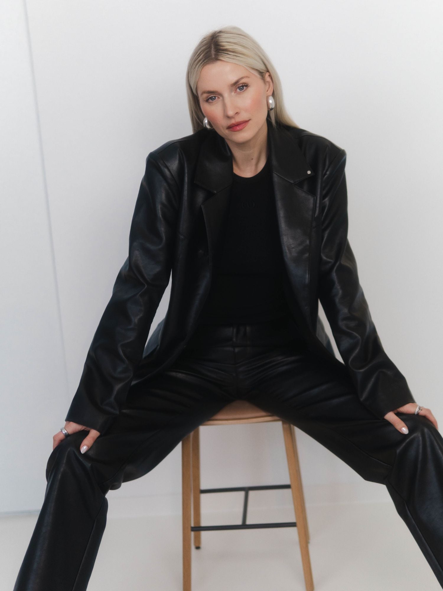 Eine Frau mit glattem blondem Haar trägt den Insa Blazer von LeGer by Lena Gercke und die dazu passende Hose. Sie sitzt auf einem Holzhocker vor einem schlichten weißen Hintergrund und schaut selbstbewusst in die Kamera.