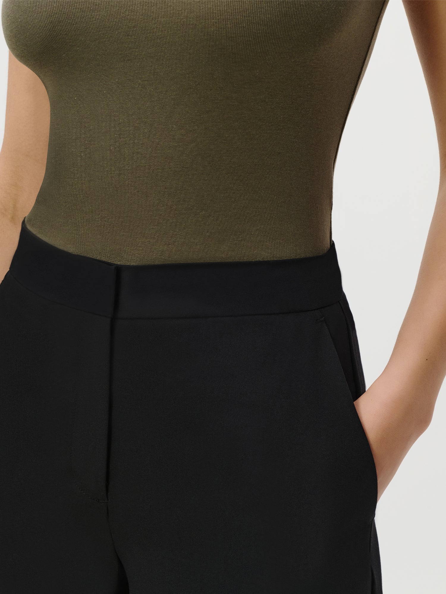 Eine Person trägt ein tailliertes, ärmelloses olivgrünes Top mit der Therese Pants Tall in Schwarz von LeGer by Lena Gercke. Der High-Waisted-Look kontrastiert stilvoll mit eleganten langen Damenkleidern oder einem Maxi Kleid, ideal für Größe 36.