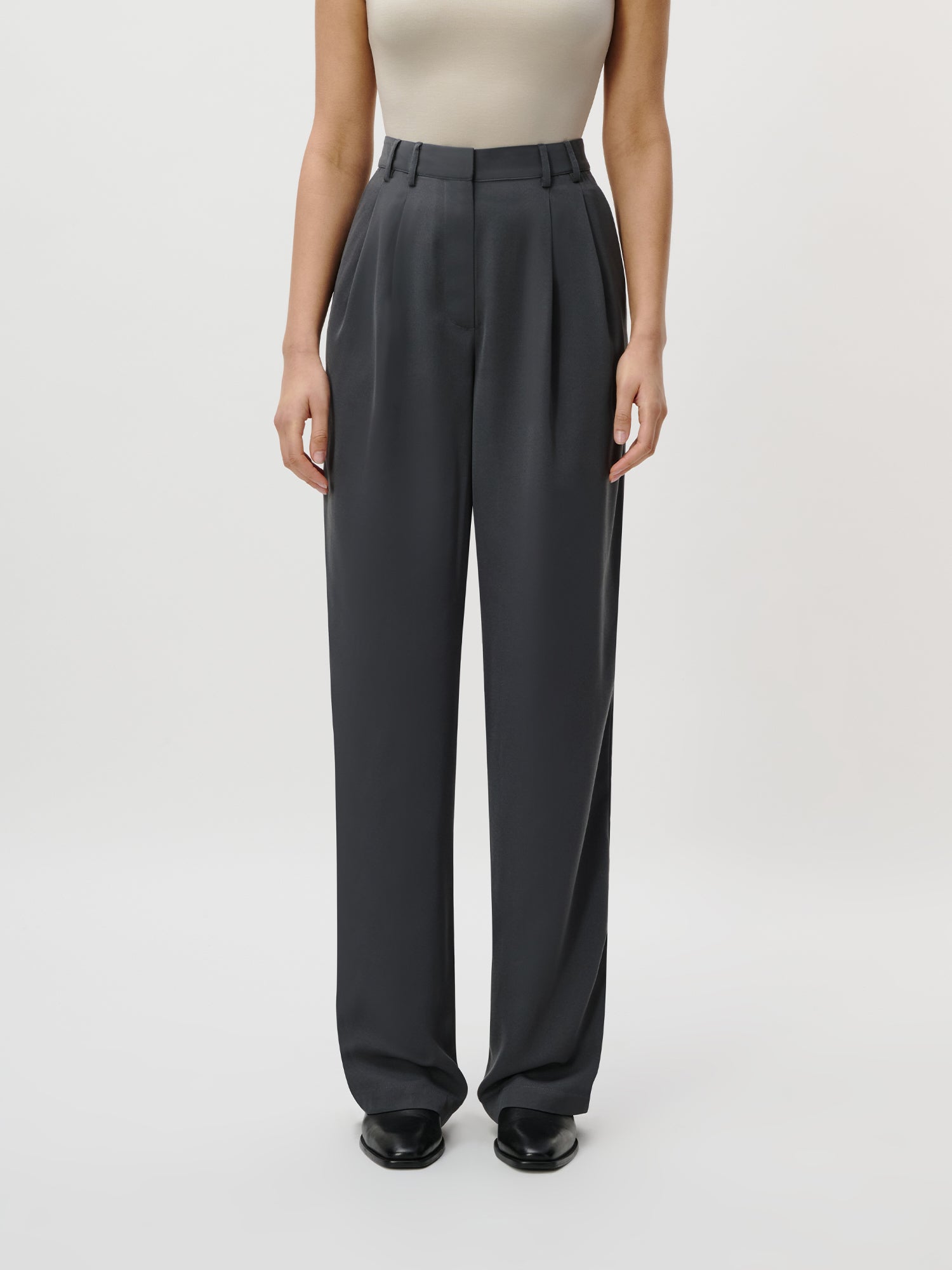 Eine Person trägt die hochtaillierte, dunkelgraue Kora Pants Tall von LeGer by Lena Gercke mit einem hellen, ärmellosen Top und schwarzen Schuhen vor einem schlichten weißen Hintergrund - ein vielseitiger Look, der ein Damenkleid oder ein langes Maxikleid ergänzt.
