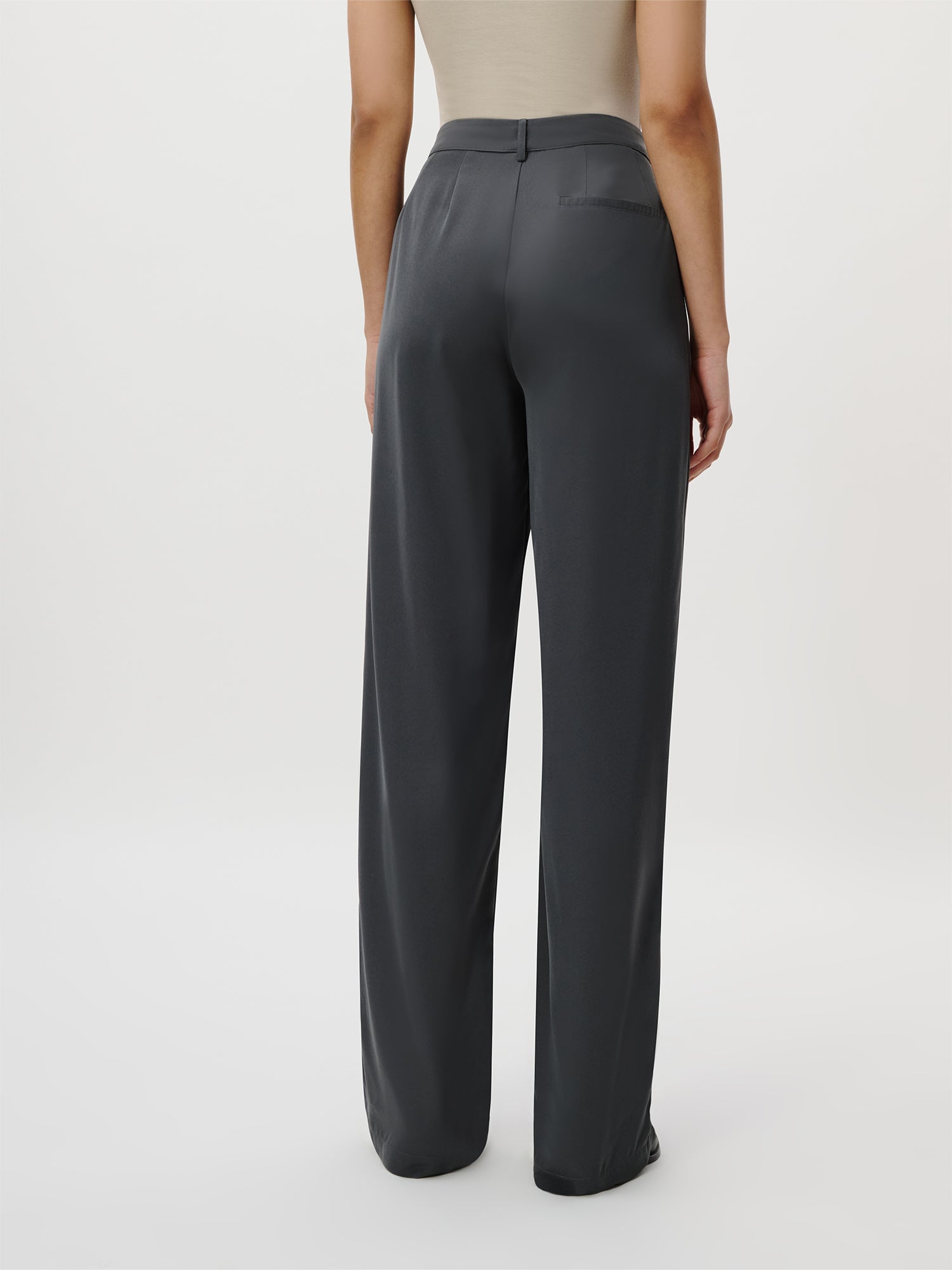 Eine Person modelliert die Kora Pants Tall von LeGer by Lena Gercke - eine lockere, dunkelgraue Hose mit hoher Taille - in Kombination mit einem beigefarbenen, ärmellosen Oberteil, das vor einem weißen Hintergrund eine schicke Alternative zum Damenkleid darstellt.