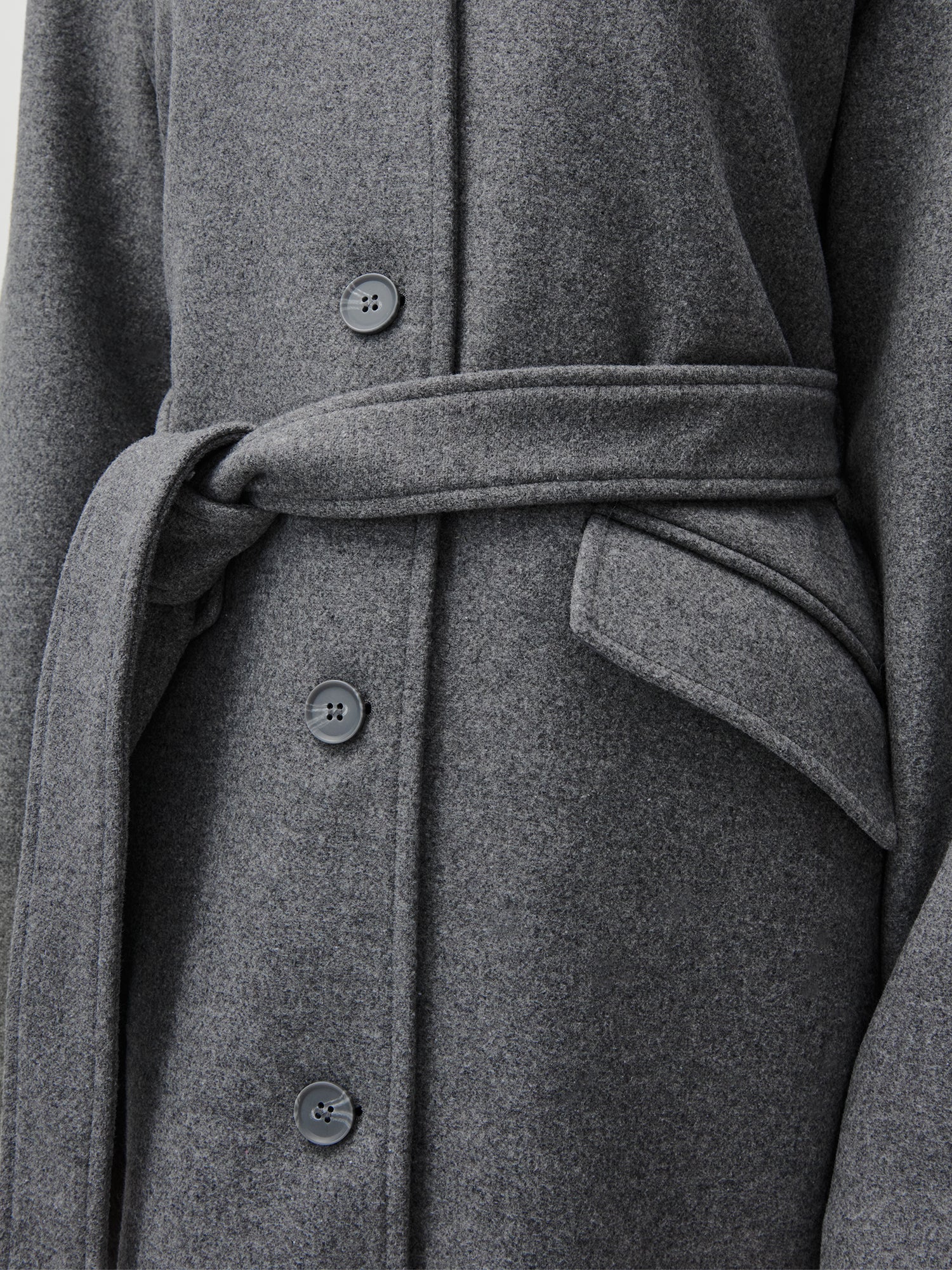 Nahaufnahme des Anaida Coat von LeGer by Lena Gercke: ein grauer Wollmantel in entspannter Passform mit vier schwarzen Knöpfen, passendem Stoffgürtel in der Taille, Taschenklappe auf der rechten Seite und schicken langen Ärmeln.