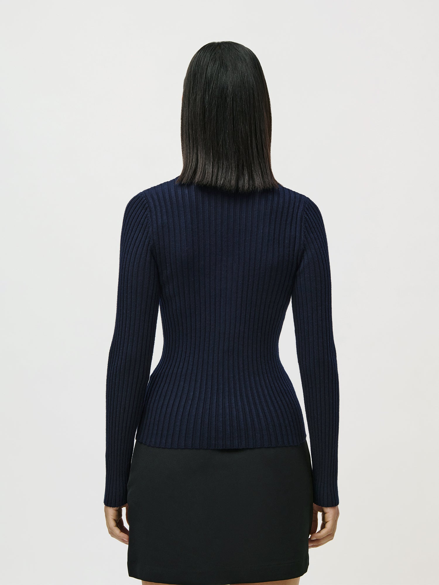 Eine Frau mit glattem, schulterlangem, dunklem Haar blickt in die Ferne. Sie trägt den LeGer by Lena Gercke Nannette Longsleeve navy ribbed sweater und einen schwarzen Rock vor einem schlichten weißen Hintergrund.