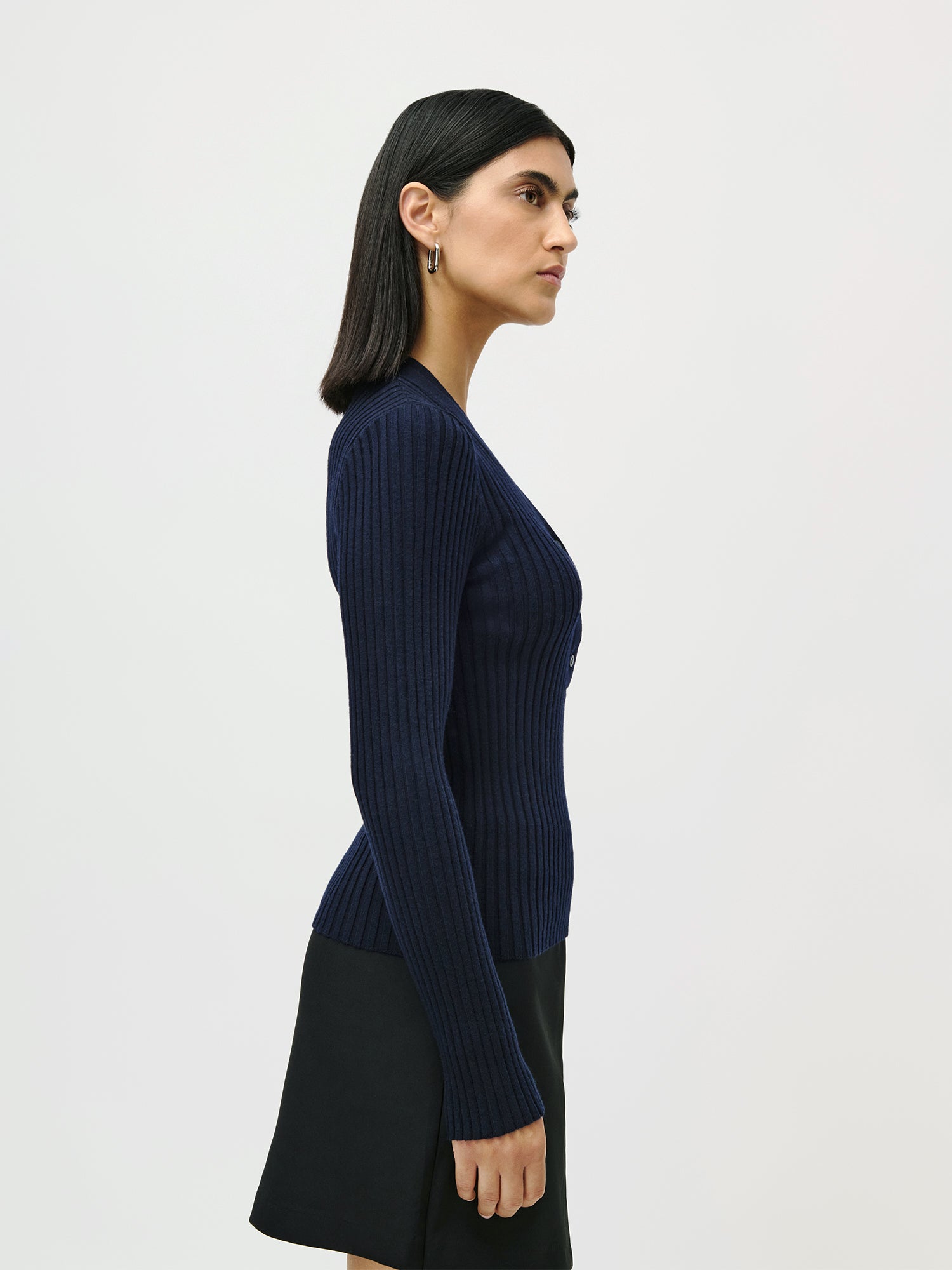 Eine Frau mit glattem schwarzem Haar, die ein marineblaues LeGer by Lena Gercke Nannette Longsleeve-Top und einen schwarzen Rock trägt, steht im Profil vor einem schlichten weißen Hintergrund.