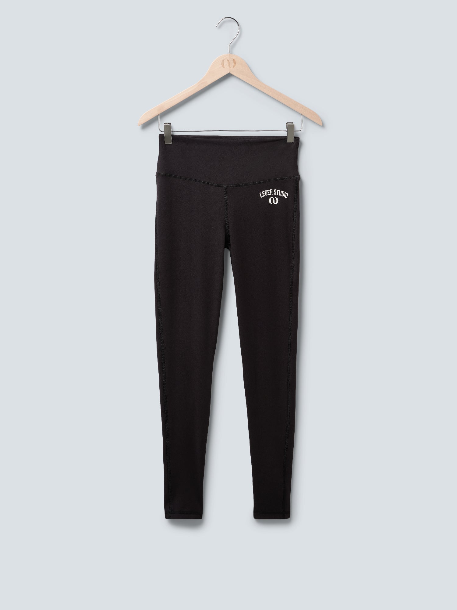 Eine schwarze Elfi Pants von LeGer by Lena Gercke hängt auf einem Holzbügel vor einem hellgrauen Hintergrund. Sie hat eine hohe Taille und ein kleines weißes "Leder Studio"-Logo auf dem oberen linken Oberschenkel.