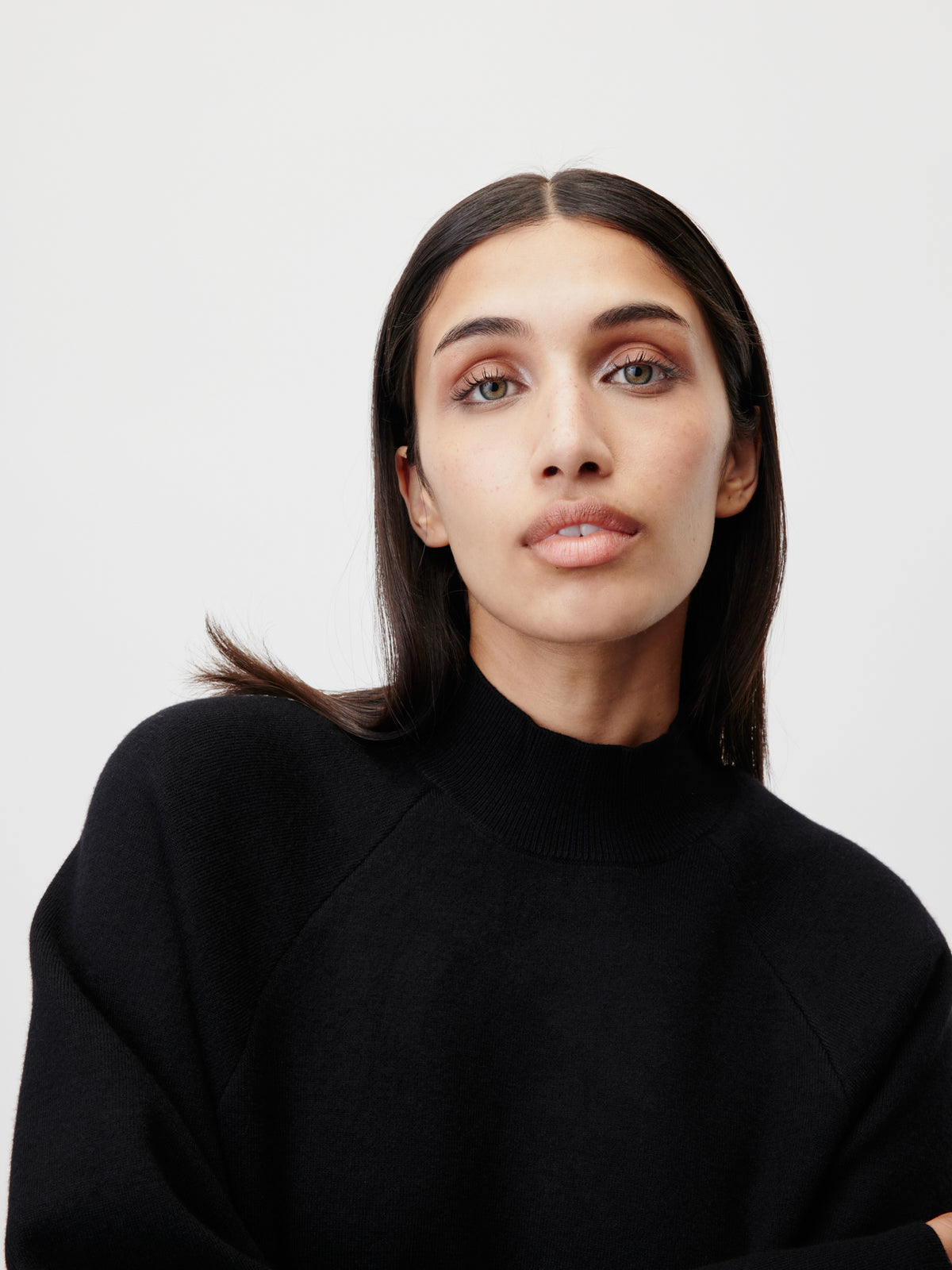 Eine Person mit langen, dunklen Haaren, die den Pullover „Heather“ von LeGer by Lena Gercke mit Raglanärmeln trägt, blickt mit neutralem Gesichtsausdruck vor einem schlichten weißen Hintergrund leicht nach oben.