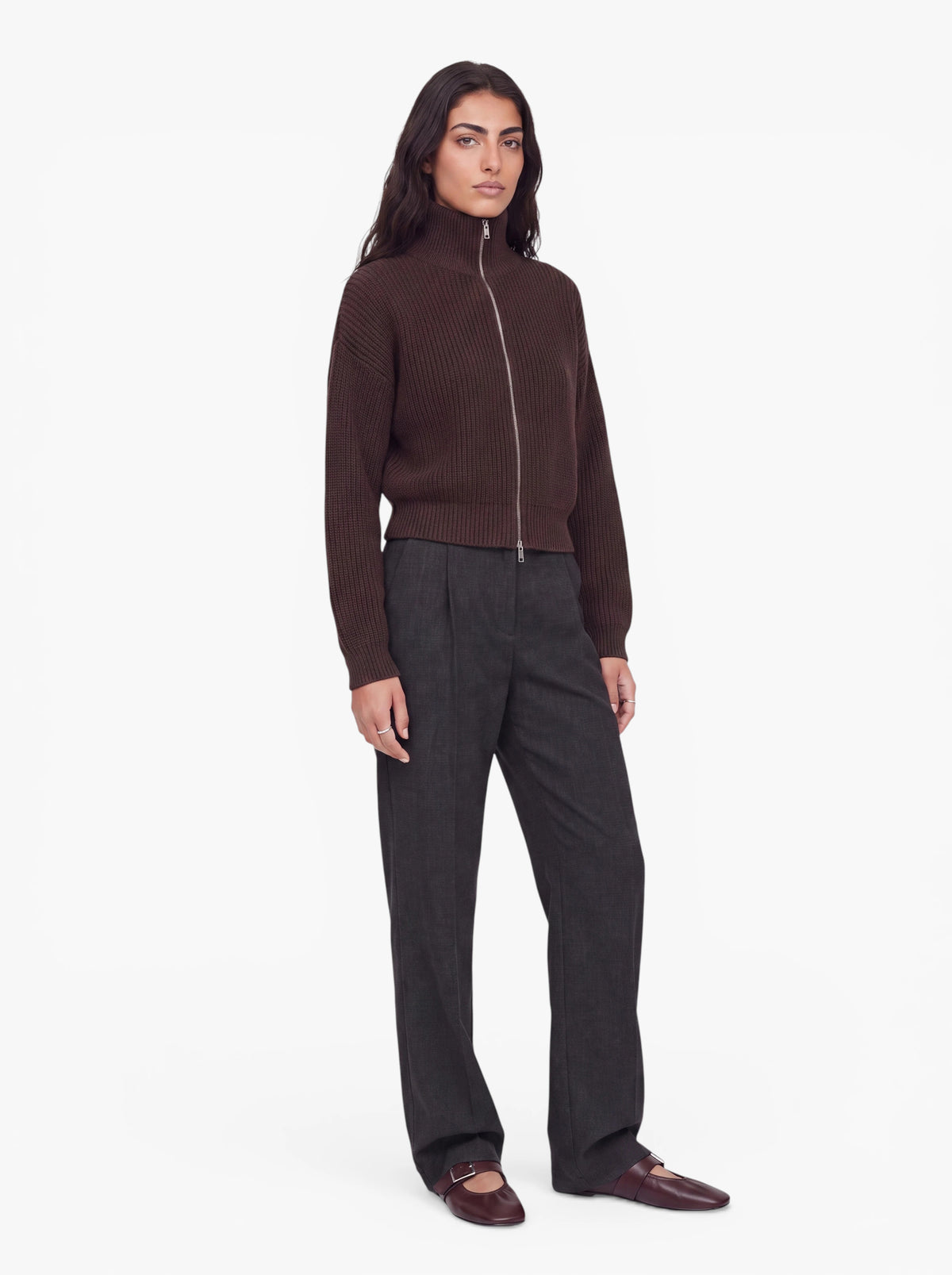 Eine Person steht mit dem Gesicht nach vorne vor einem schlichten weißen Hintergrund und trägt den Pullover „Cindy“ von LeGer by Lena Gercke in brauner Rippstrickoptik mit Reißverschluss, eine graue Hose mit geradem Bein sowie dunkelbraune Schuhe.