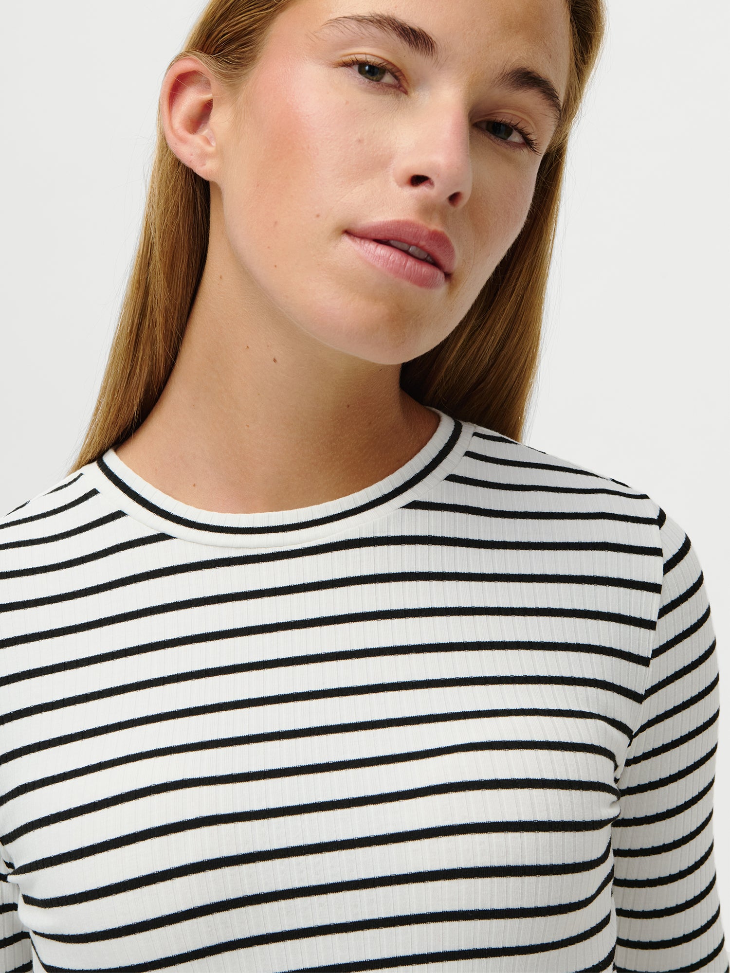 Eine Person mit langem, glattem, hellbraunem Haar trägt das Cinzia Longsleeve by LeGer by Lena Gercke - ein schmales, weißes, langärmeliges Hemd mit schwarzen Querstreifen - vor einem schlichten weißen Hintergrund und blickt leicht in die Kamera.