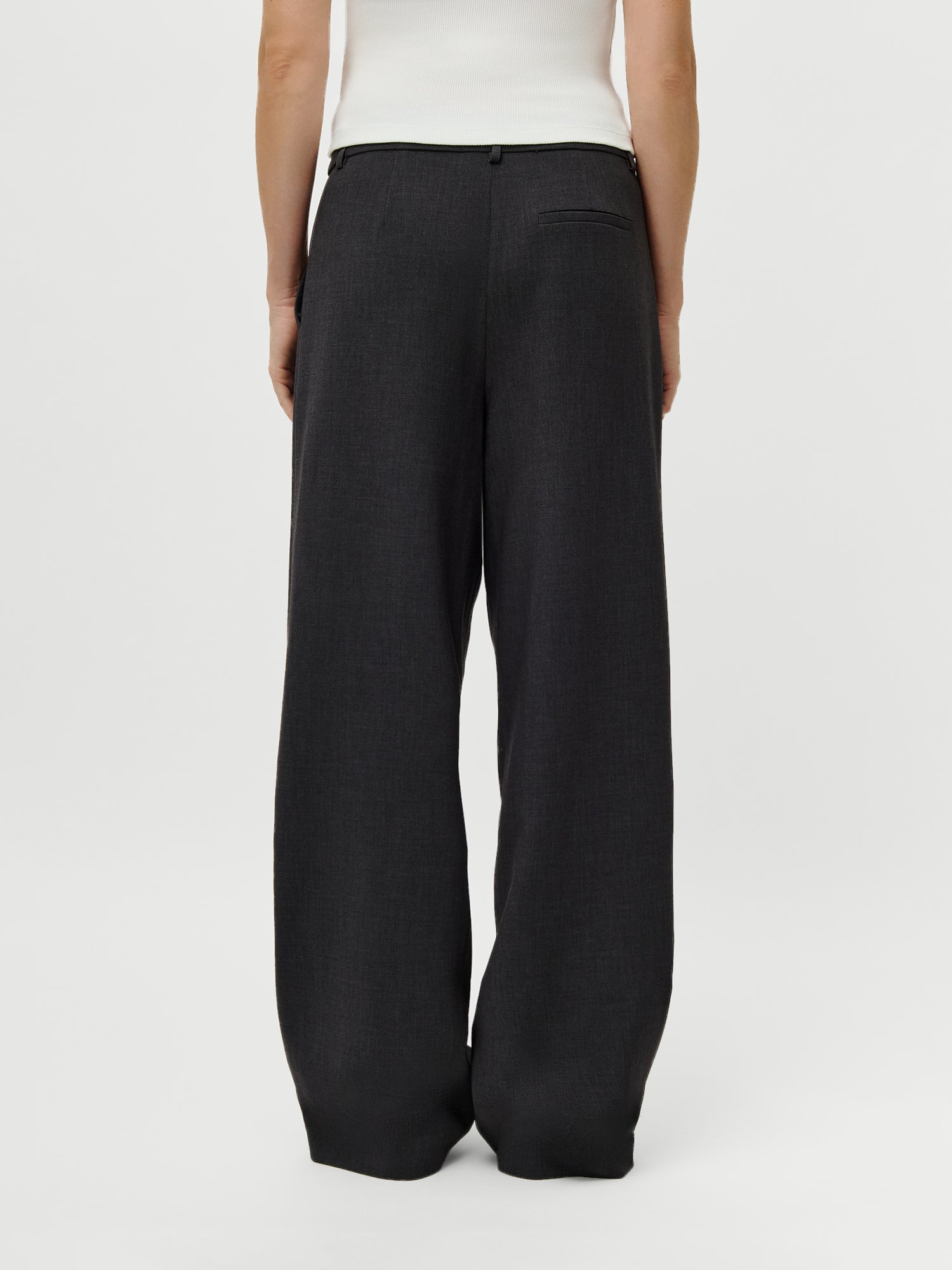 Abgebildet ist eine Person von hinten in der LeGer x Oh April - Franja Pants Tall von LeGer by Lena Gercke in dunkelgrau (Größe 38), gepaart mit einem weißen ärmellosen Oberteil, gestylt in moderner damenmode, vor einem schlichten weißen Hintergrund.