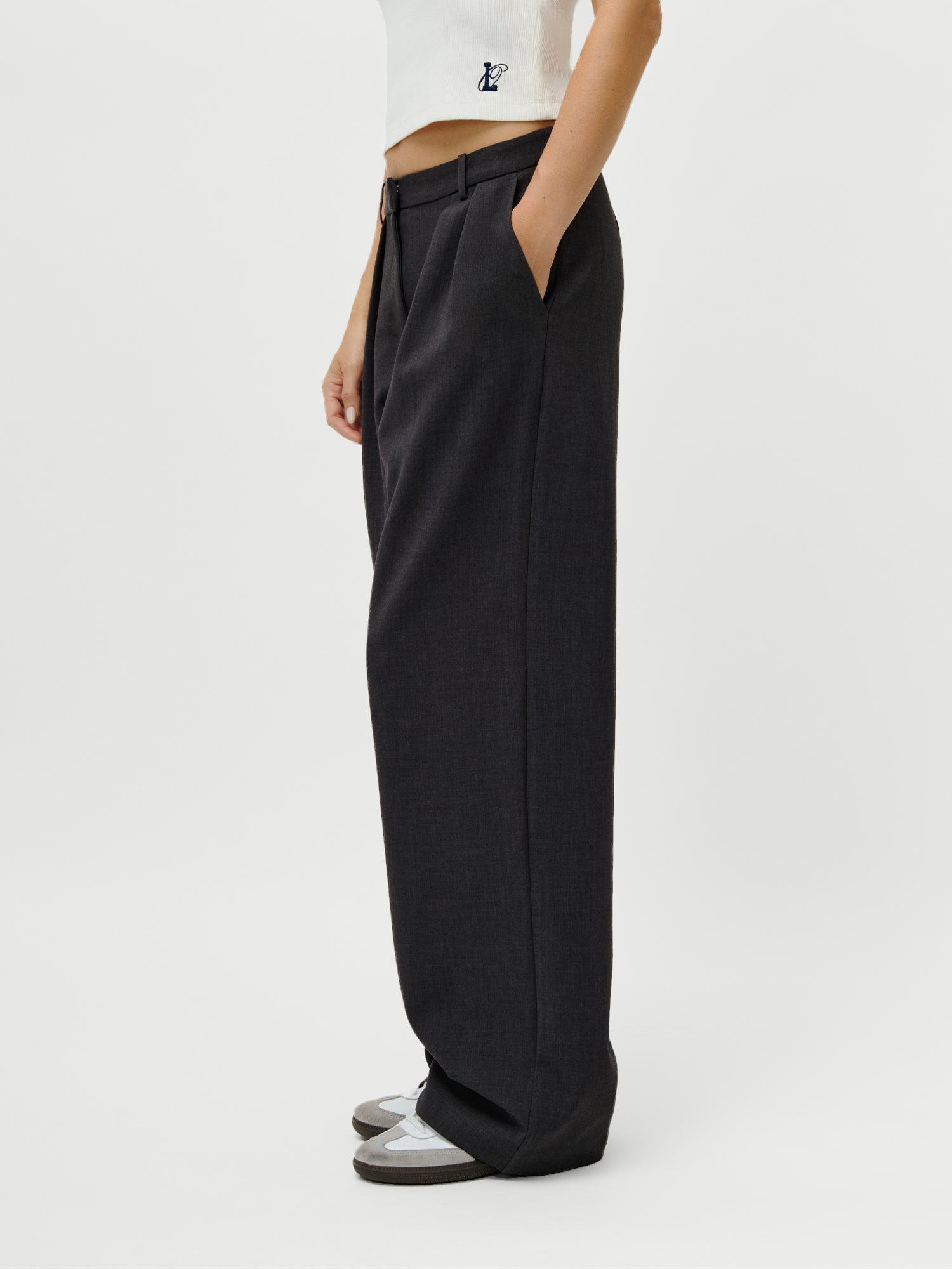 Eine Person modelliert die LeGer x Oh April Franja Pants Tall von LeGer by Lena Gercke in Größe 38, gepaart mit einem weißen Oberteil und Turnschuhen, und posiert mit den Händen in den Taschen vor einem schlichten weißen Hintergrund.