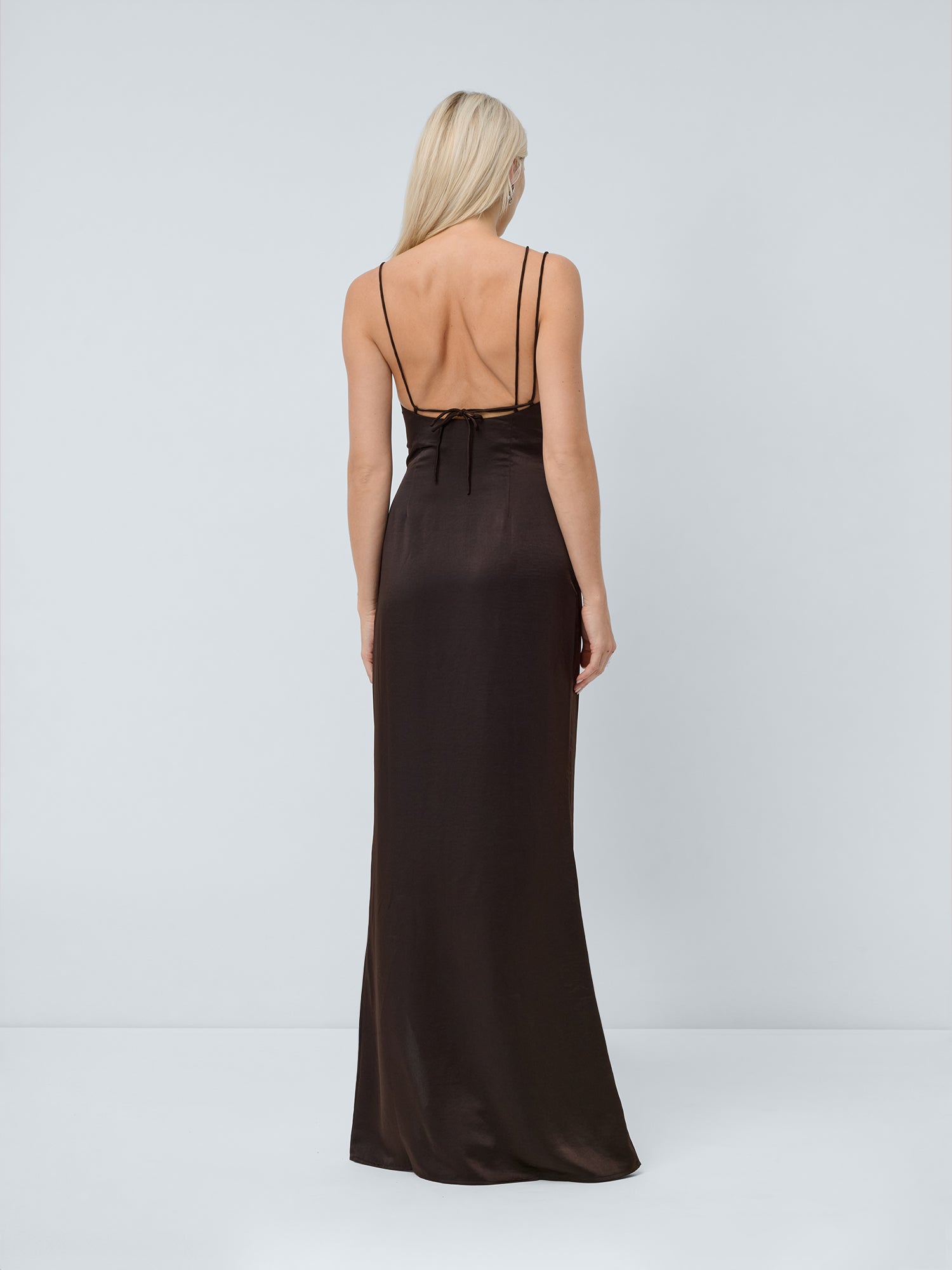 Rückansicht einer blonden Frau im Kleid „Lena“ von LeGer by Lena Gercke, einem dunkelbraunen Maxikleid aus Satin mit schmaler Passform, Spaghettiträgern und tiefem Rückenausschnitt mit Bindedetail.