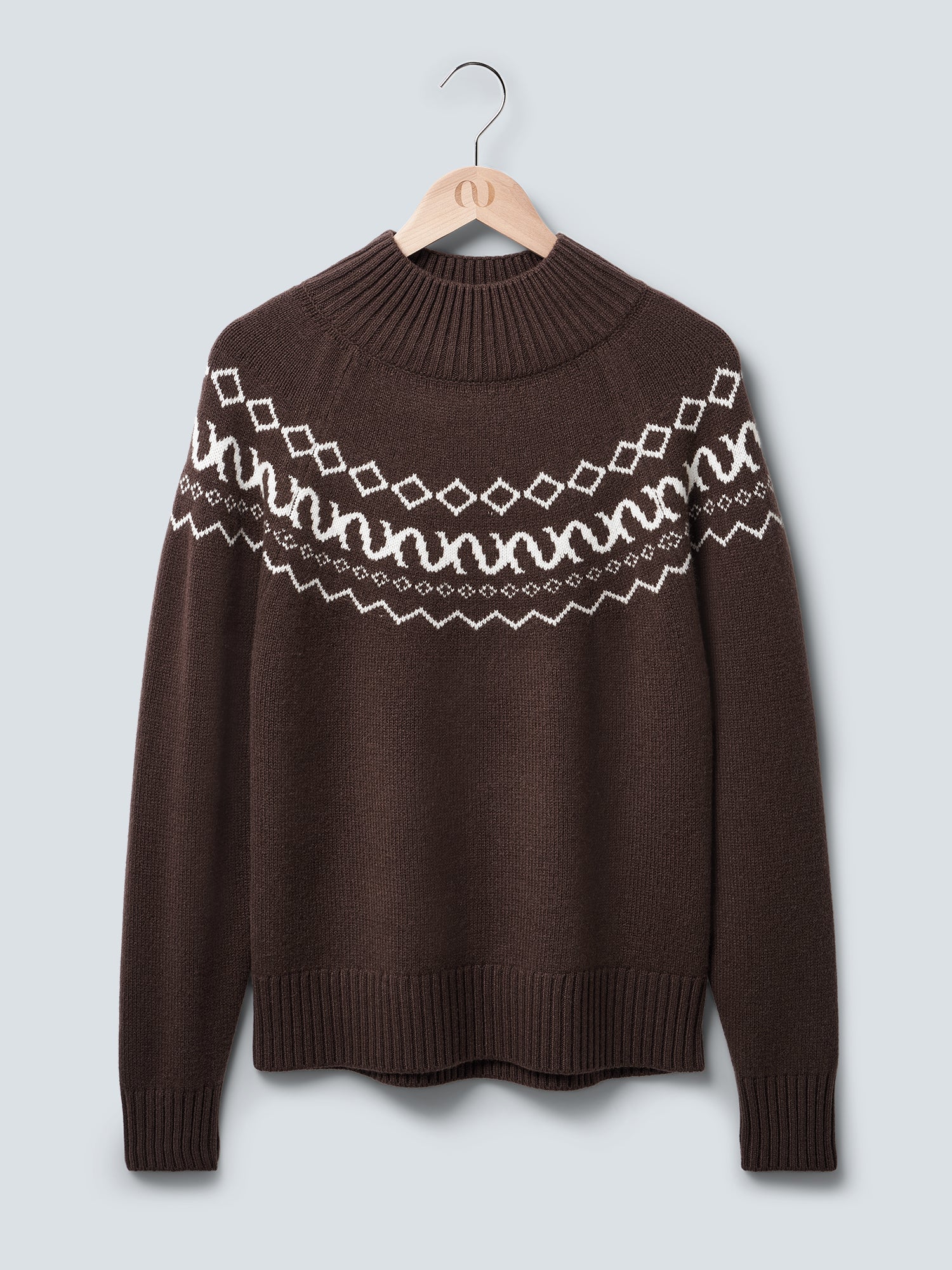 Der Hellen Pullover von LeGer by Lena Gercke ist ein dunkelbrauner Strickpullover mit einem weißen geometrischen Muster auf der Brust und den oberen Ärmeln, der auf einem Holzbügel vor einem hellgrauen Hintergrund gezeigt wird.