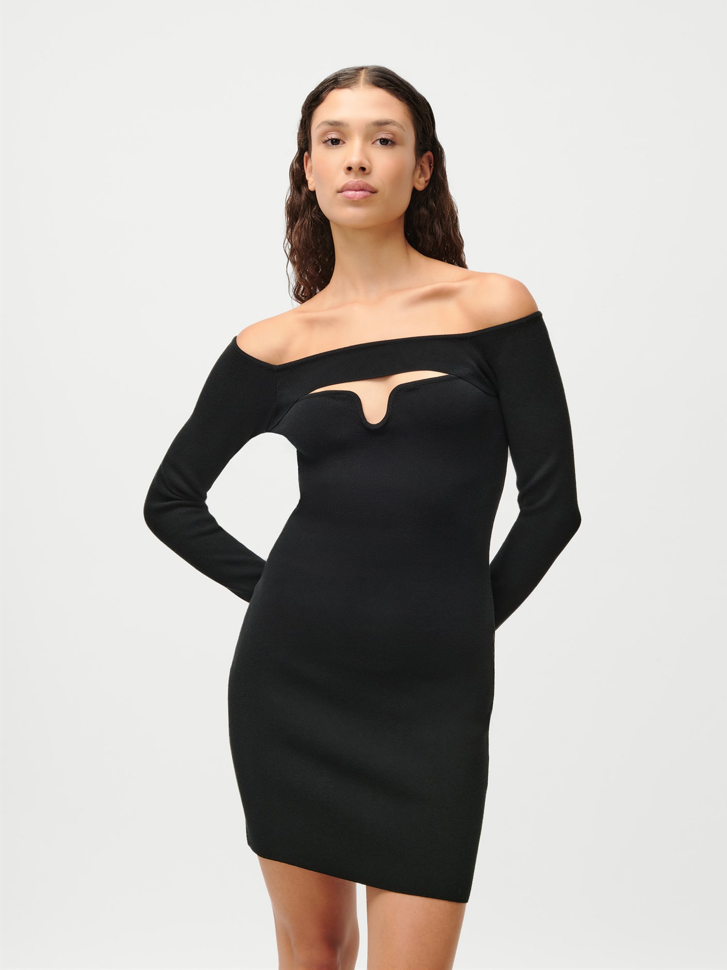 Eine Frau mit langen, gewellten braunen Haaren trägt das LeGer by Lena Gercke Evelin Dress - ein schmal geschnittenes, schulterfreies schwarzes Minikleid mit einem Ausschnitt auf der Vorderseite -, das vor einem schlichten weißen Hintergrund steht und mit neutralem Blick in die Kamera schaut.