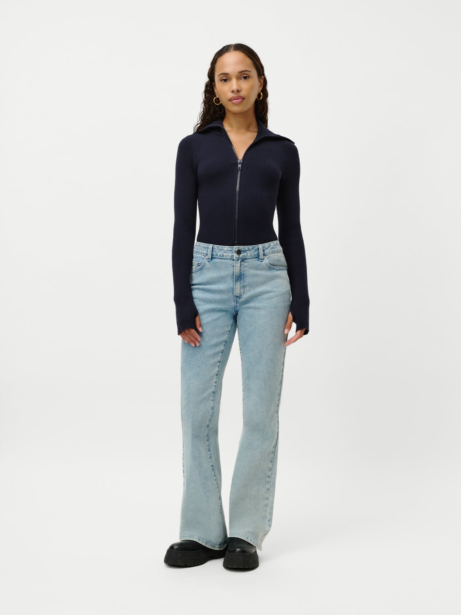 Eine Frau blickt nach vorne und trägt den Heidi Body by LeGer by Lena Gercke in Marineblau mit langen Ärmeln und Reißverschluss vorne, gepaart mit hellblauen Jeans in normaler Länge und schwarzen Schuhen, vor einem schlichten weißen Hintergrund.