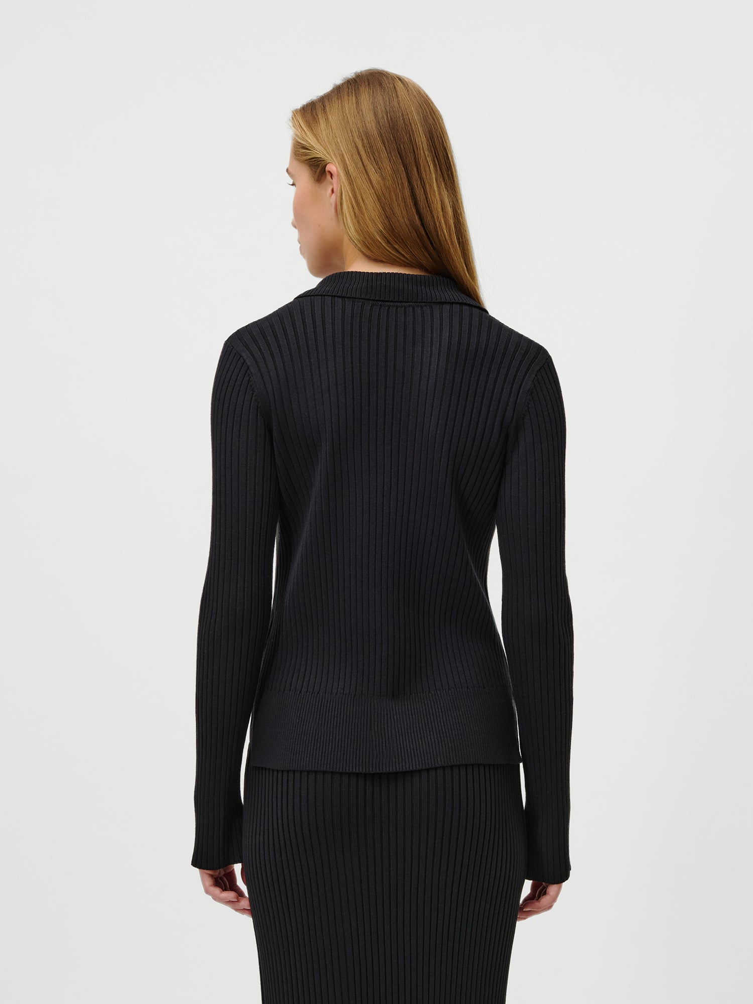 Eine Frau mit glattem, hellbraunem Haar ist von hinten zu sehen. Sie trägt den Charlotte Pullover von LeGer by Lena Gercke in Schwarz, mit extra langen Ärmeln und normaler Passform in Größe 36, vor einem schlichten weißen Hintergrund.