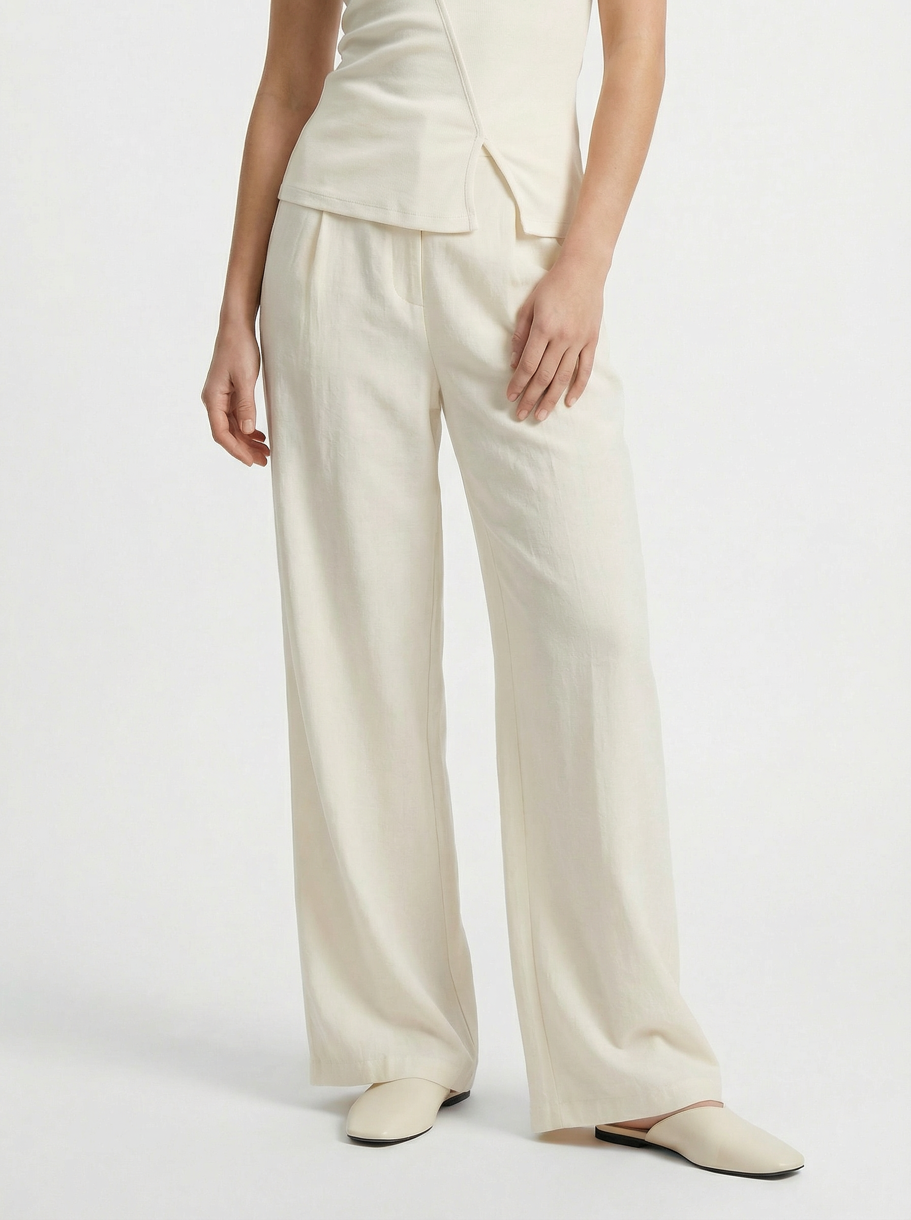 Die untere Hälfte einer Person ist in der Thorina Pants in Creme von LeGer by Lena Gercke, gepaart mit einem passenden Maxitop und cremefarbenen Flats, vor einem schlichten weißen Hintergrund zu sehen.
