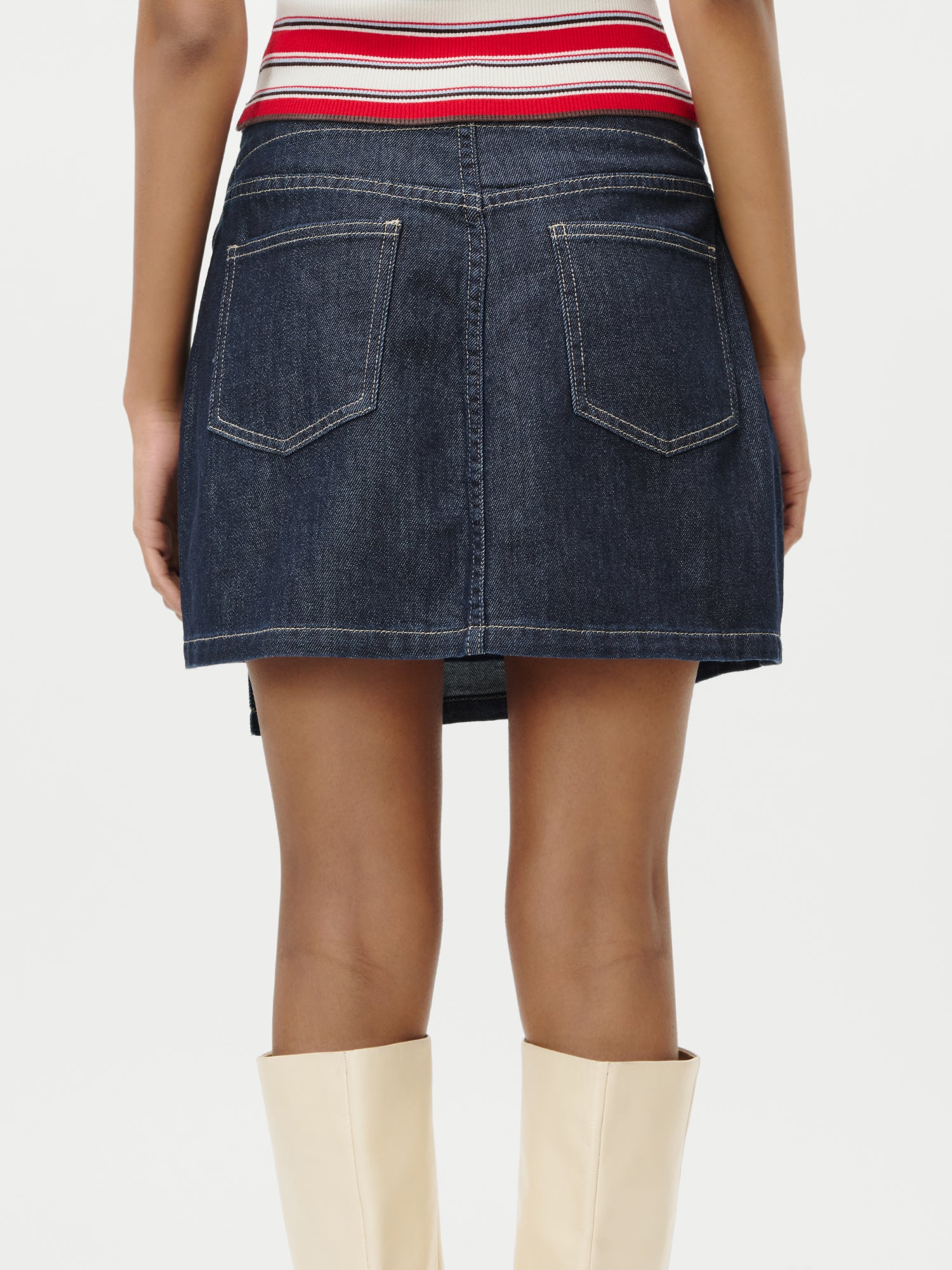 Eine Person, die den dunkelblauen Swantje Rock von LeGer by Lena Gercke mit Gesäßtaschen, ein gestreiftes Oberteil und cremefarbene kniehohe Stiefel trägt, wird von hinten vor einem einfarbig weißen Hintergrund gezeigt.