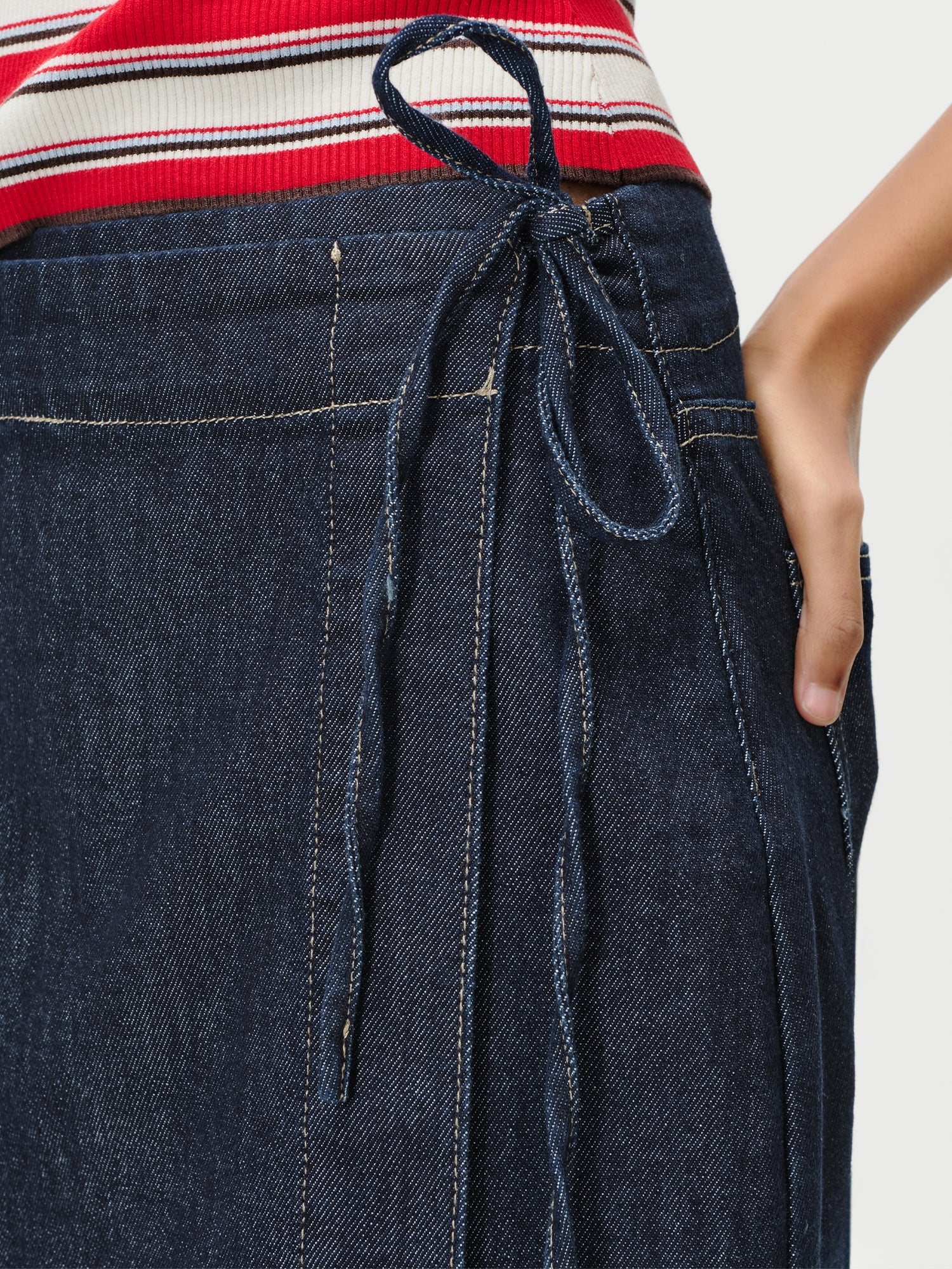 Nahaufnahme einer Person, die den dunkelblauen High-Waist-Rock „Swantje“ von LeGer by Lena Gercke mit seitlichem Bindeband trägt und die Hand in die Tasche gesteckt hat; dazu ein rot-weiß-rosa gestreiftes Oberteil.