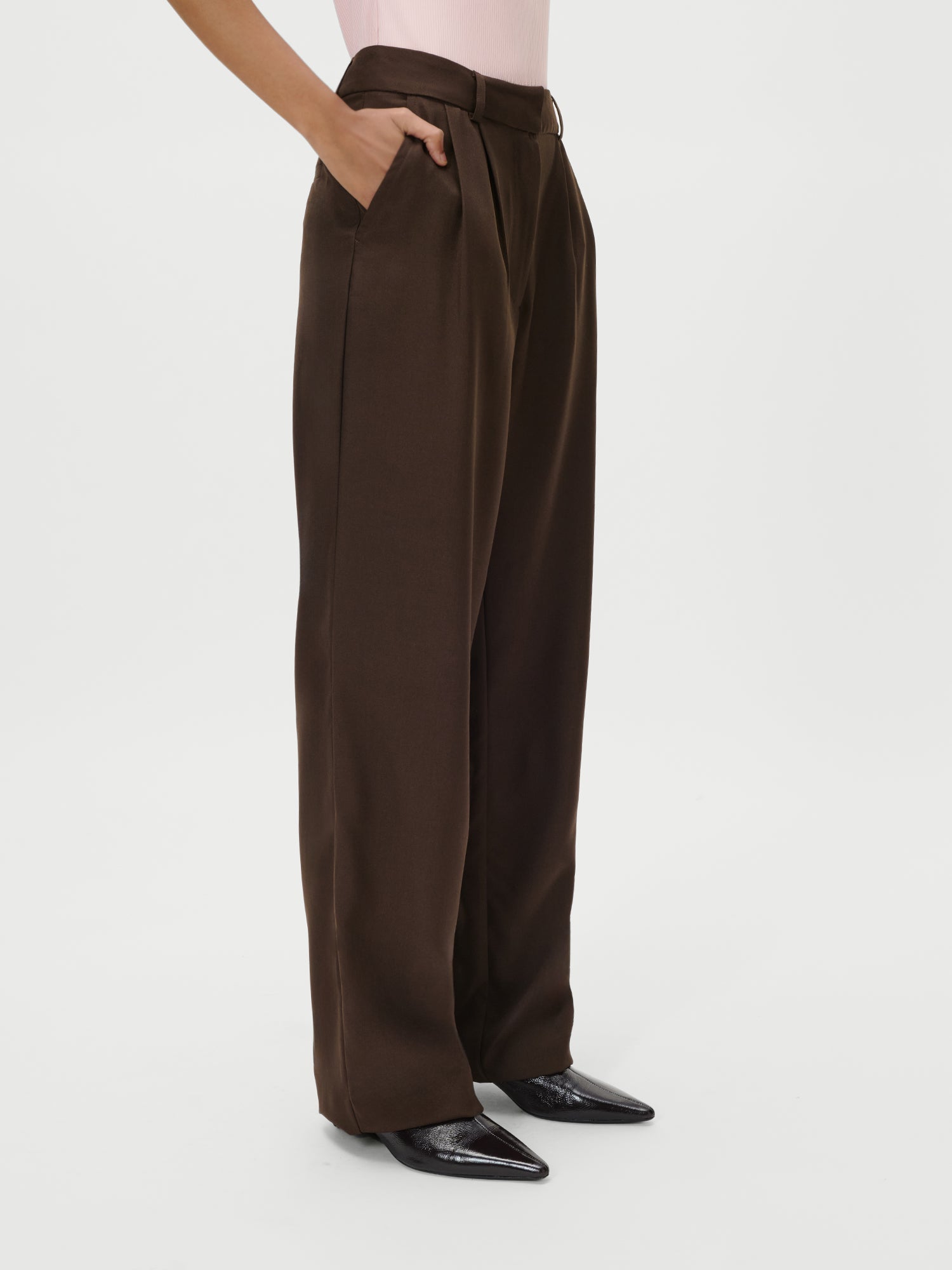 Eine Person trägt die Jerika Pants von LeGer by Lena Gercke - eine braune Hose mit hoher Taille, weitem Bein und Taschen -, die mit einem hellrosa Oberteil und spitzen schwarzen Schuhen vor weißem Hintergrund kombiniert wird; ideal, um sie mit einem Maxikleid in Größe 36 zu kombinieren.