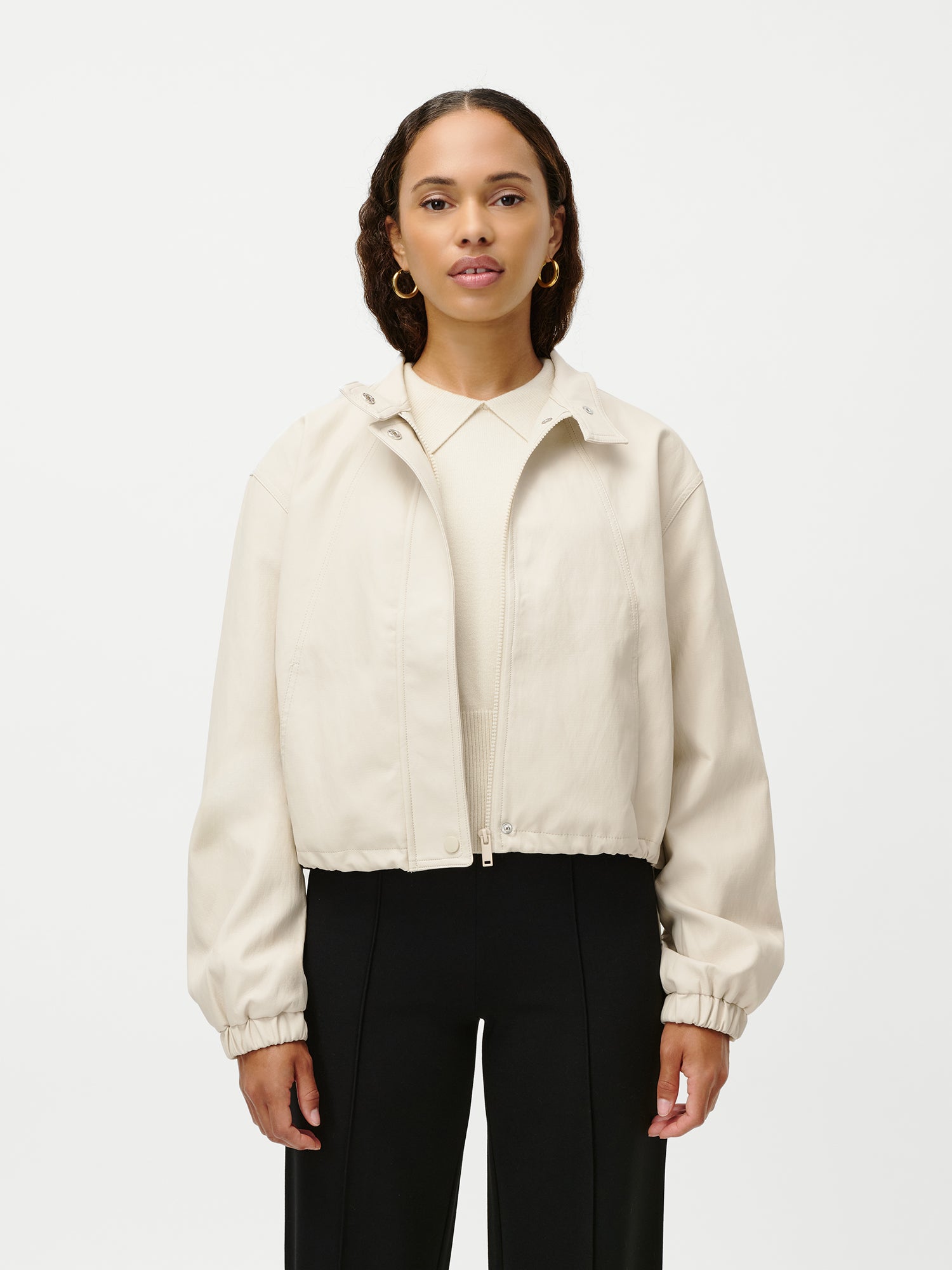 Eine Frau blickt nach vorne und trägt eine LeGer by Lena Gercke Janet Jacket, eine hellbeige, langärmelige Jacke mit Reißverschluss, über einem cremefarbenen Top und einer schwarzen Hose. Sie trägt goldene Ohrringe und ihr Haar in lockeren Wellen. Hier in Größe 36 vor weißem Hintergrund abgebildet.