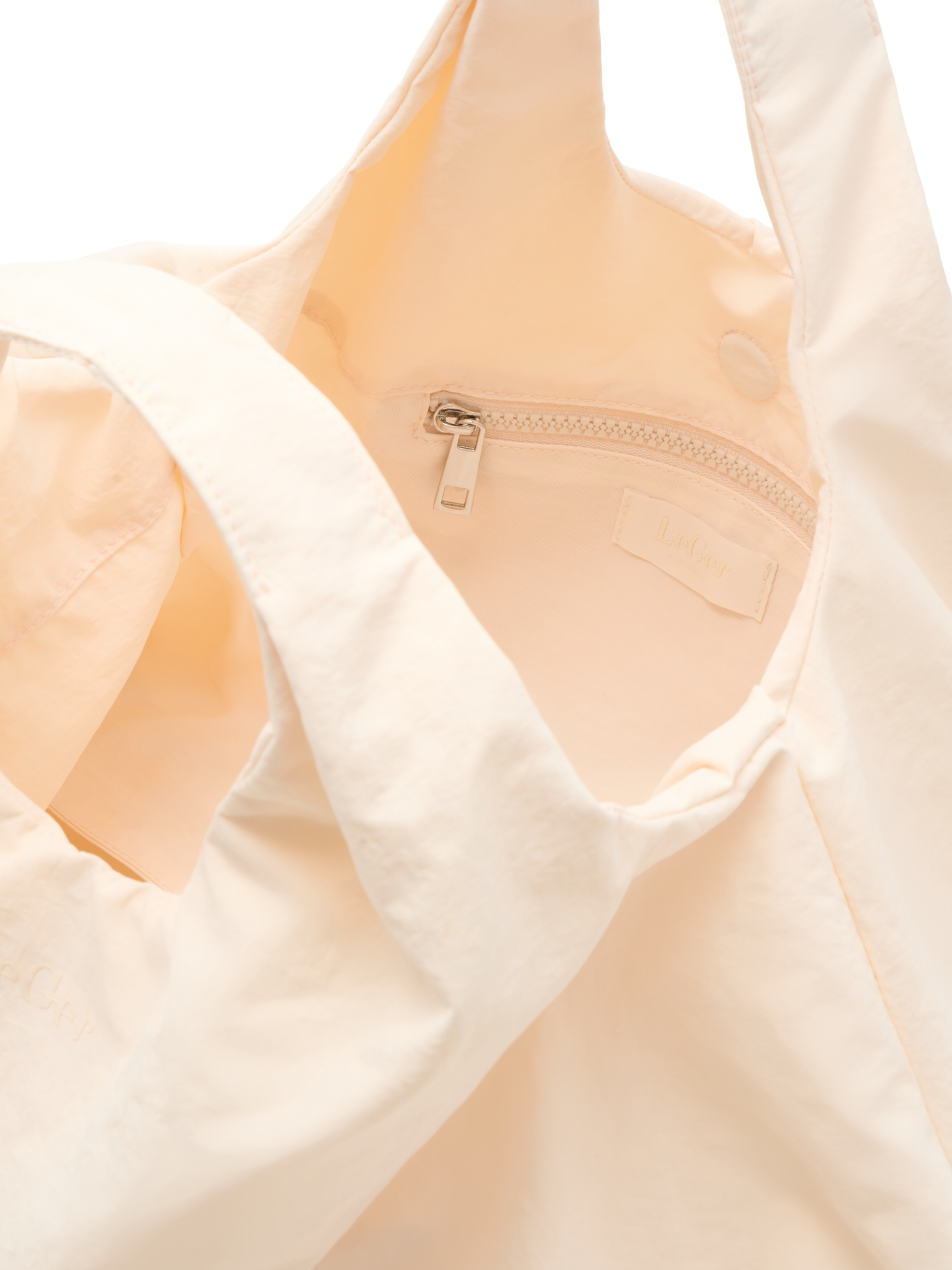 Eine Nahaufnahme der Lotti Bag von LeGer by Lena Gercke zeigt ihr weiches, leicht cremefarbenes Material, eine Innentasche mit Reißverschluss und ein Stoffetikett im Inneren.