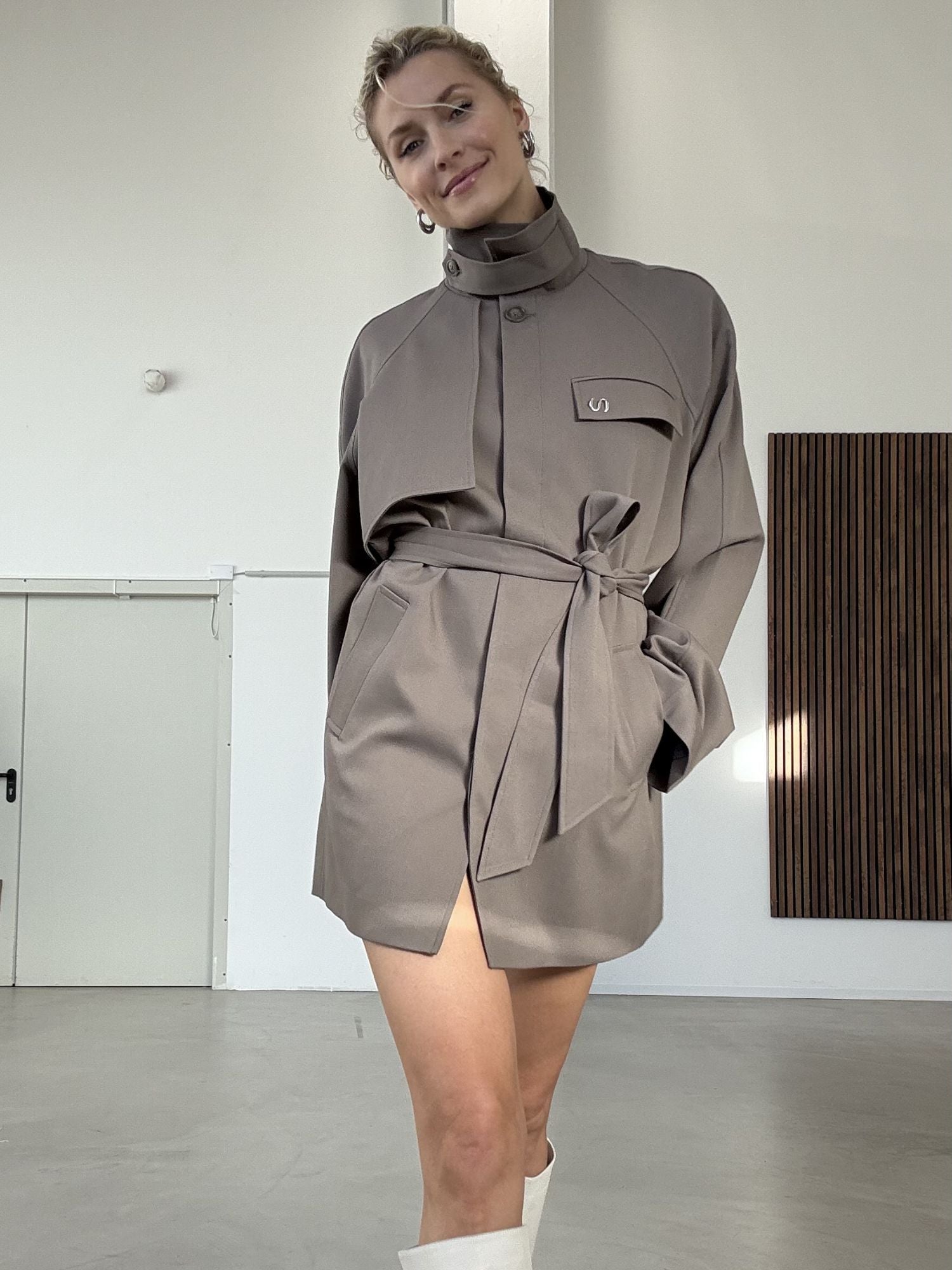 Eine Frau, die die Fee Jacket von LeGer by Lena Gercke trägt, steht in einem minimalistischen Innenraum mit weißen Wänden und modernem Dekor und lächelt leicht in die Kamera.