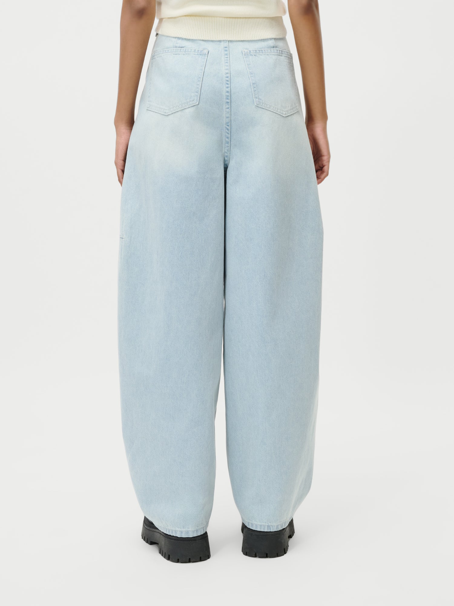 Eine Person ist von hinten zu sehen, die LeGer by Lena Gercke Eilika Pants in Hellblau und schwarze Schuhe mit klobigen Sohlen trägt - ideal für lässige Looks, die sich leicht mit Maxi- oder langen Kleidern in Größe 36 vor einem schlichten weißen Hintergrund kombinieren lassen.