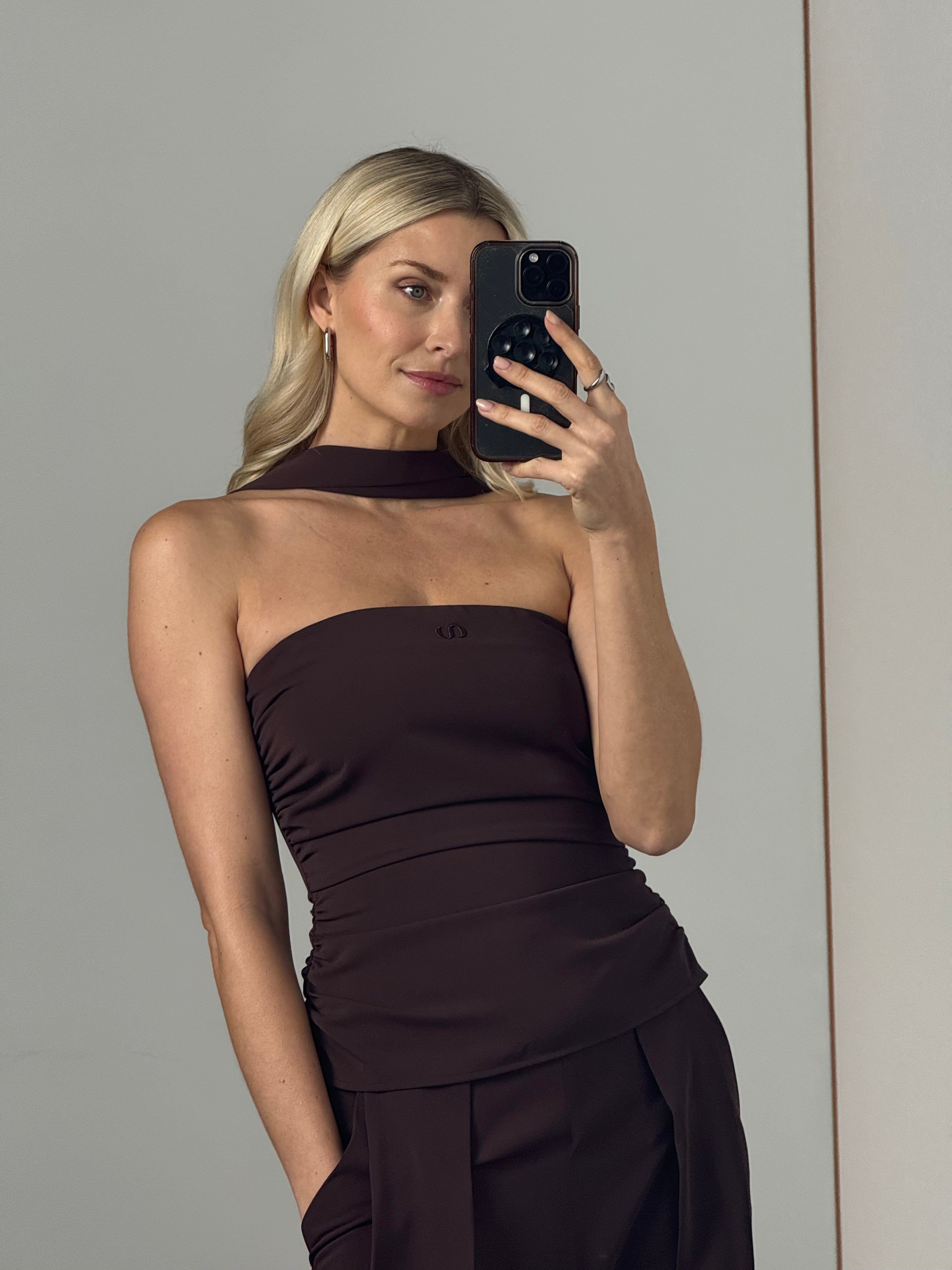 Eine blonde Frau macht ein Selfie im Spiegel und trägt dabei das Christina Set von LeGer by Lena Gercke - ein figurbetontes Outfit mit einzigartigem Ausschnitt und passender Hose mit weitem Bein - während sie vor einem schlichten, hellen Hintergrund steht.