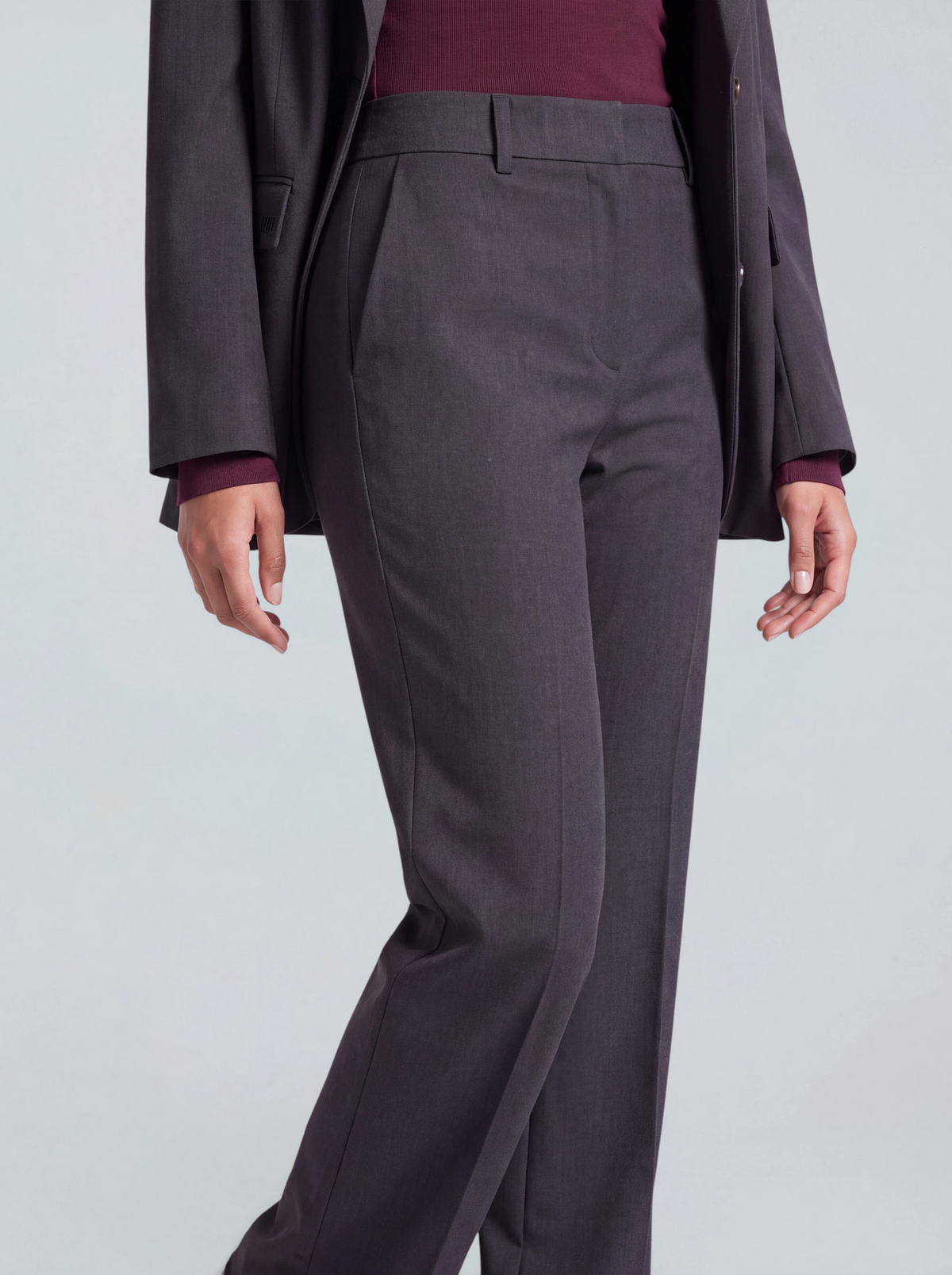 Eine Person, die eine anthrazitfarbene „Fergie“-Hose in Regular-Fit von LeGer by Lena Gercke trägt, dazu einen passenden Blazer über einem burgunderroten Oberteil, steht vor einem hellgrauen Hintergrund und posiert mit ausgestrecktem Bein.