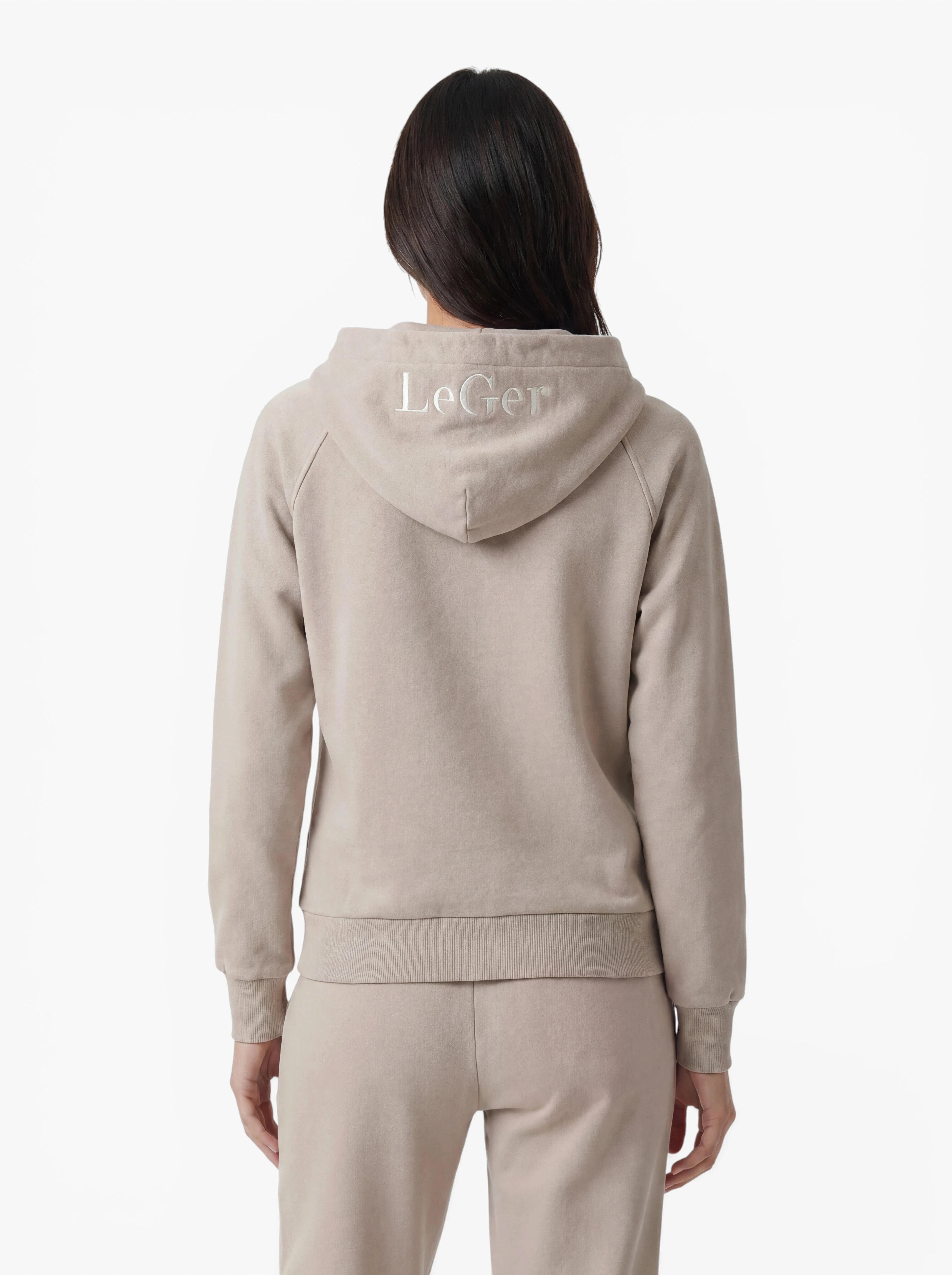 Eine Person ist von hinten zu sehen. Sie trägt den beigen „Phoenix“-Hoodie und die dazu passende Hose von LeGer by Lena Gercke – ideal für sportliche Aktivitäten oder zum Entspannen in aller Bequemlichkeit. Die Kapuze ist aufgesetzt und gibt den Blick auf den weißen „LeGer“-Stick freigibt. Der Hintergrund ist schlicht weiß.