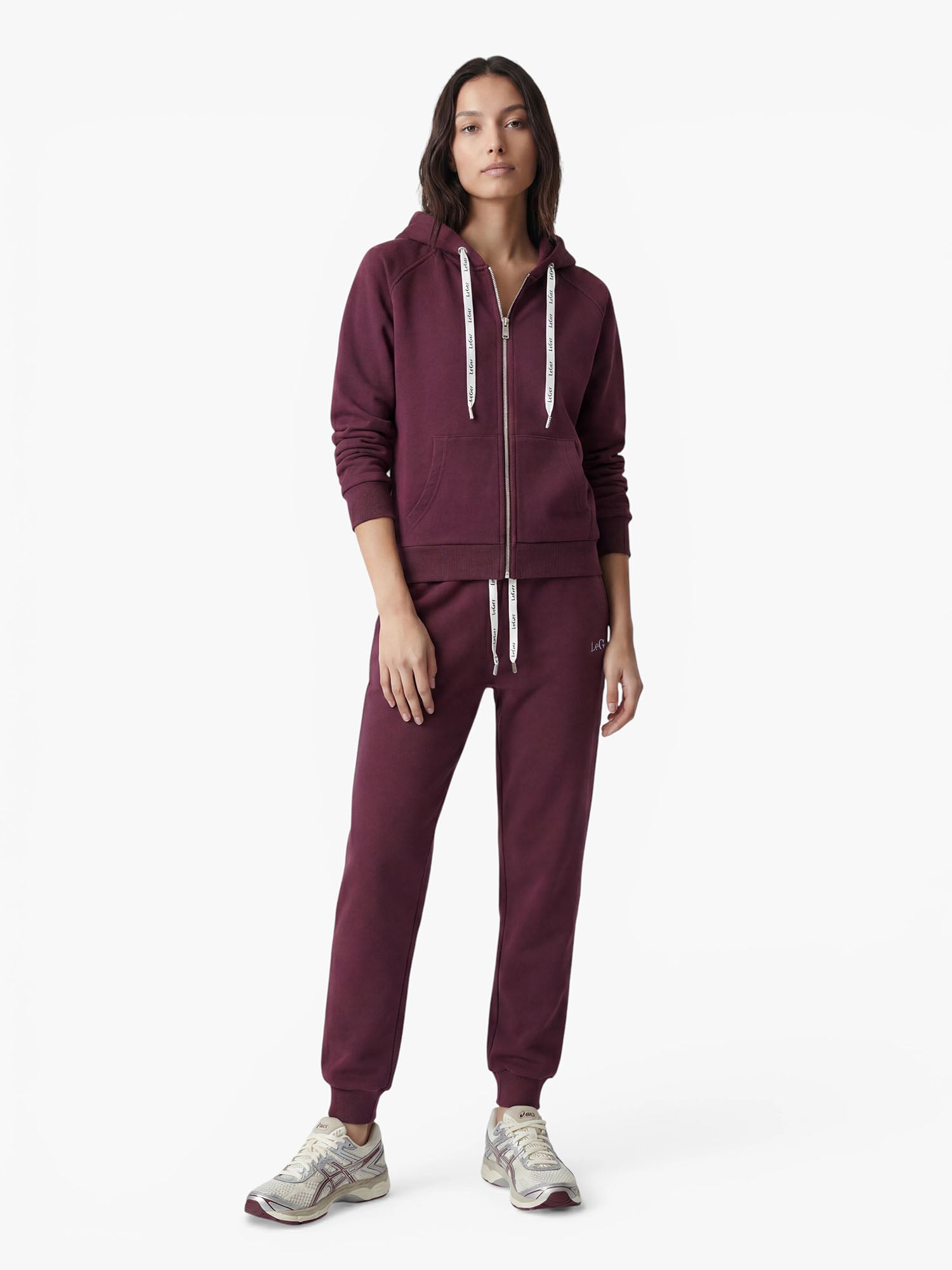 Vor einem weißen Hintergrund steht eine Person, die einen passenden burgunderroten Hoodie und eine Hose im „Nela“-Stil von LeGer by Lena Gercke mit weißen Kordeln trägt, kombiniert mit hellen Sneakers für eine schmeichelhafte Silhouette.