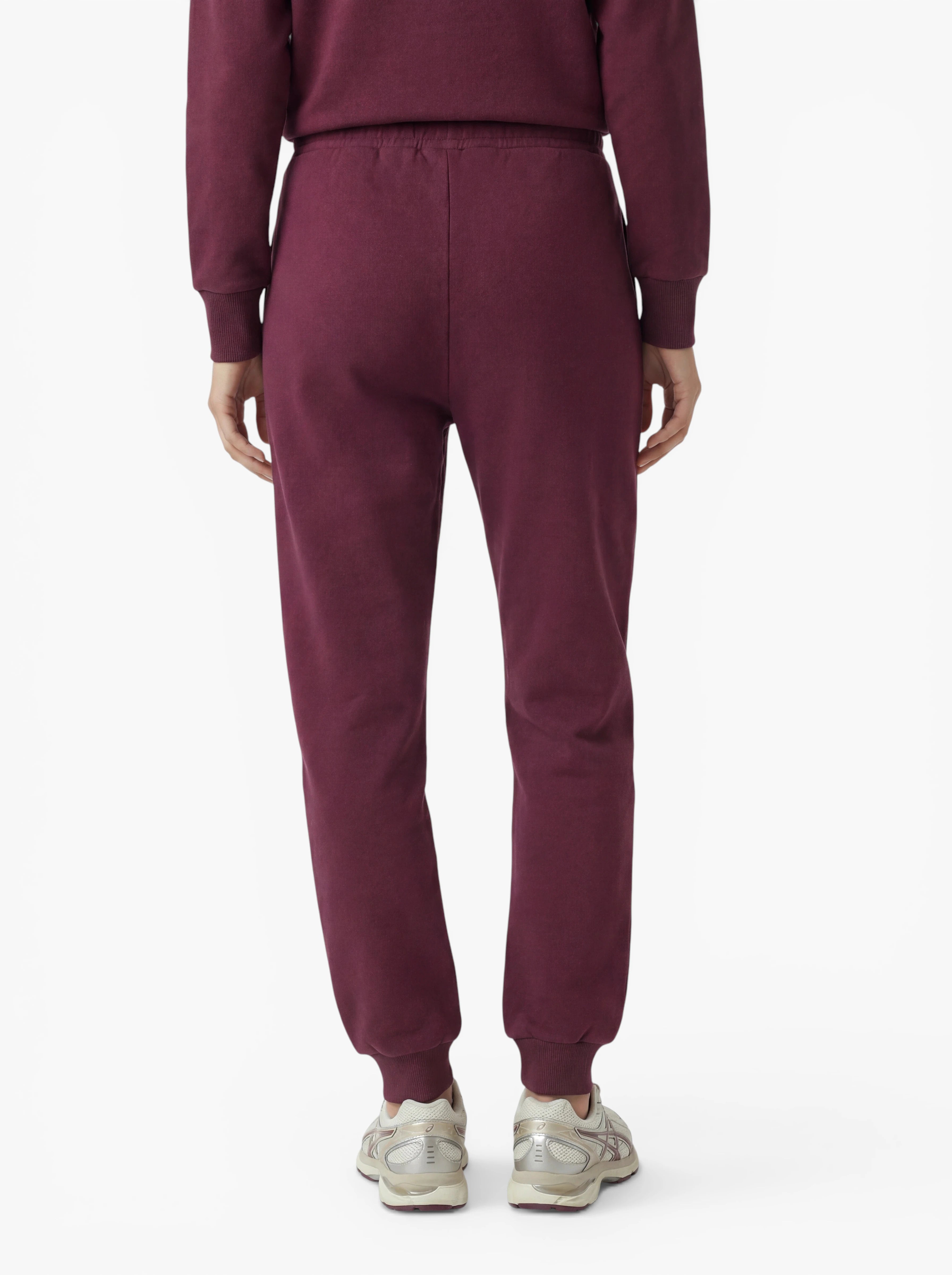 Eine Person ist von hinten zu sehen und trägt eine Hose im Modell „Nela“ von LeGer by Lena Gercke in Burgunderrot sowie ein passendes Oberteil. Diese eleganten Hosen unterstreichen eine schmeichelhafte Silhouette und werden mit klassischen weißen Sneakers kombiniert. Der Hintergrund ist einfarbig weiß.