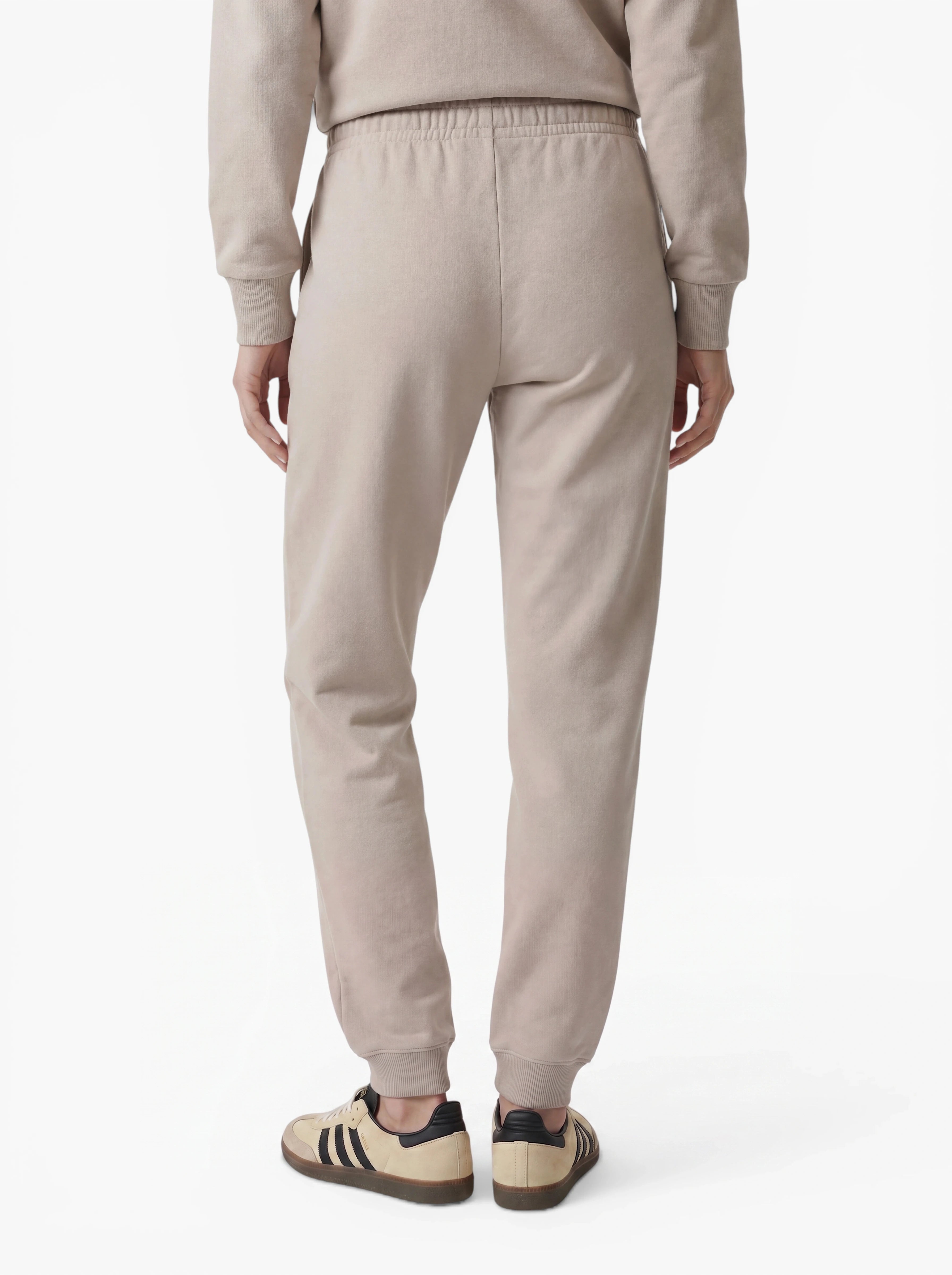 Eine Person steht mit dem Rücken zur Kamera und trägt die beigefarbene Hose „Nela“ von LeGer by Lena Gercke, die sich durch eine moderne Silhouette auszeichnet. Zu diesem vielseitigen Look kombiniert sie ein passendes Sweatshirt und beigefarbene Sneaker mit schwarzen Streifen – vor einem weißen Hintergrund entsteht so ein mühelos stilvoller Look.