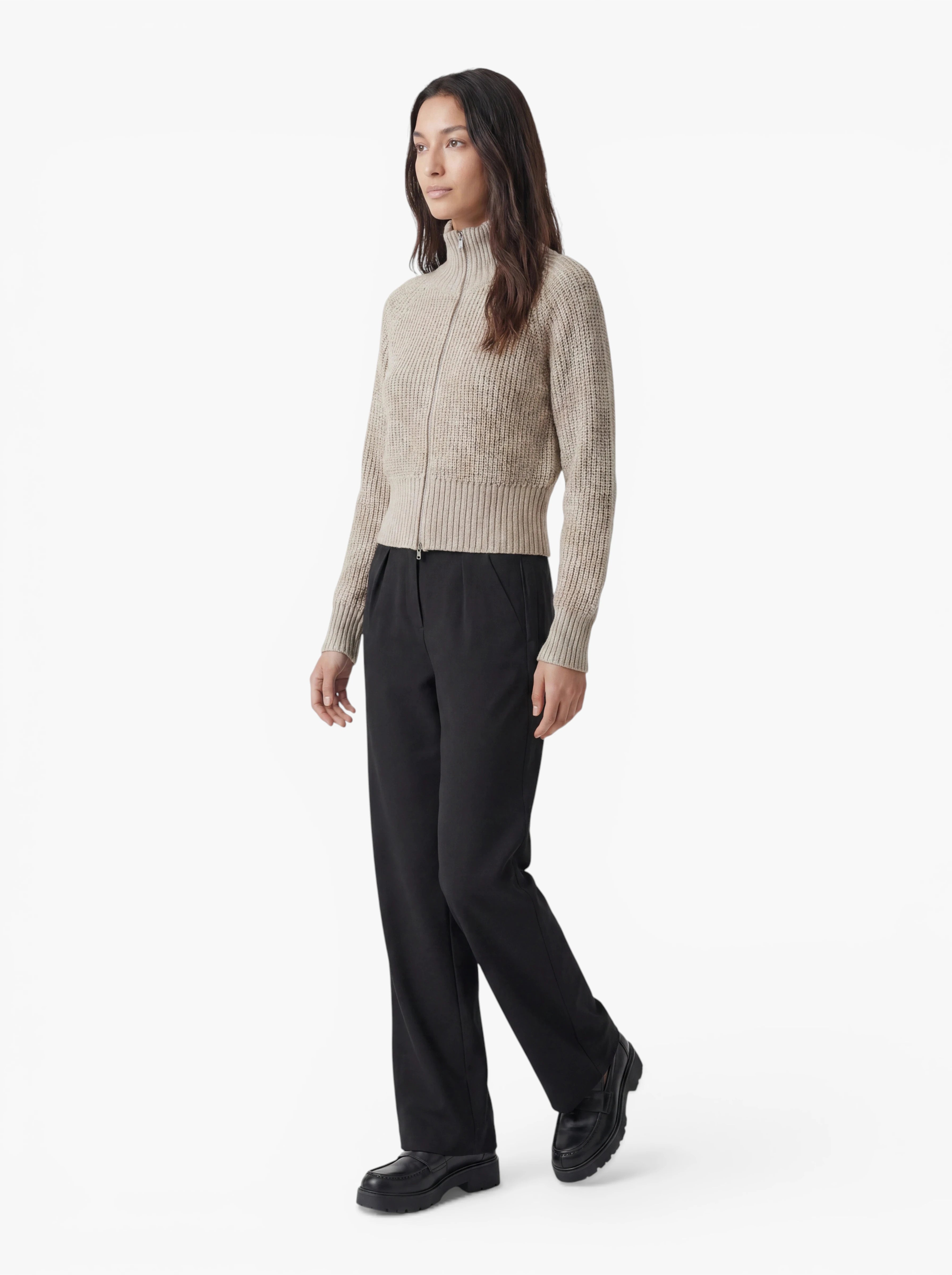 Eine Person steht vor einem weißen Hintergrund und trägt den beigen Pullover „Nala“ von LeGer by Lena Gercke, dazu eine schwarze Hose und schwarze Schuhe. Sie hat langes dunkles Haar und einen neutralen Gesichtsausdruck.