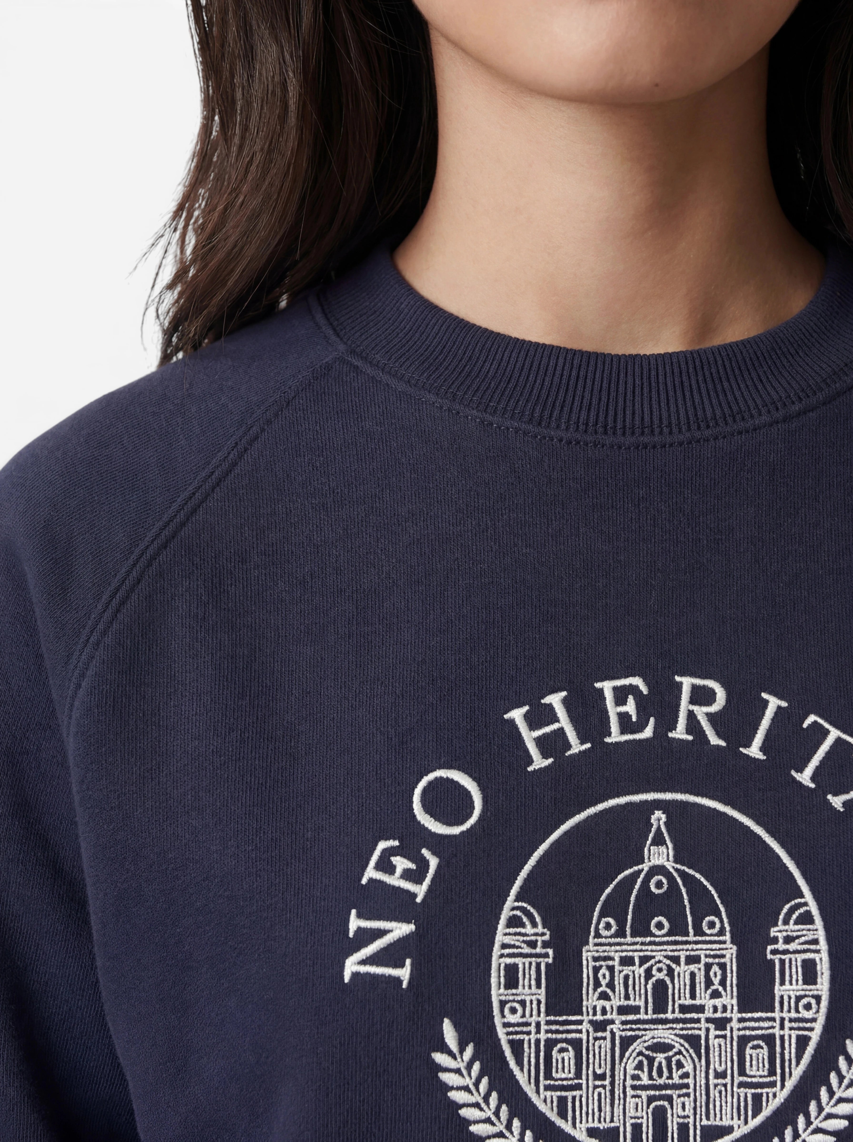 Eine Person, die den marineblauen „Bettina“-Pullover von LeGer by Lena Gercke trägt, der mit einer weißen Stickerei eines Gebäudes und dem teilweise sichtbaren Schriftzug „NEO HERIT“ verziert ist und mit seiner lockeren Passform den Casual-Stil perfekt verkörpert.