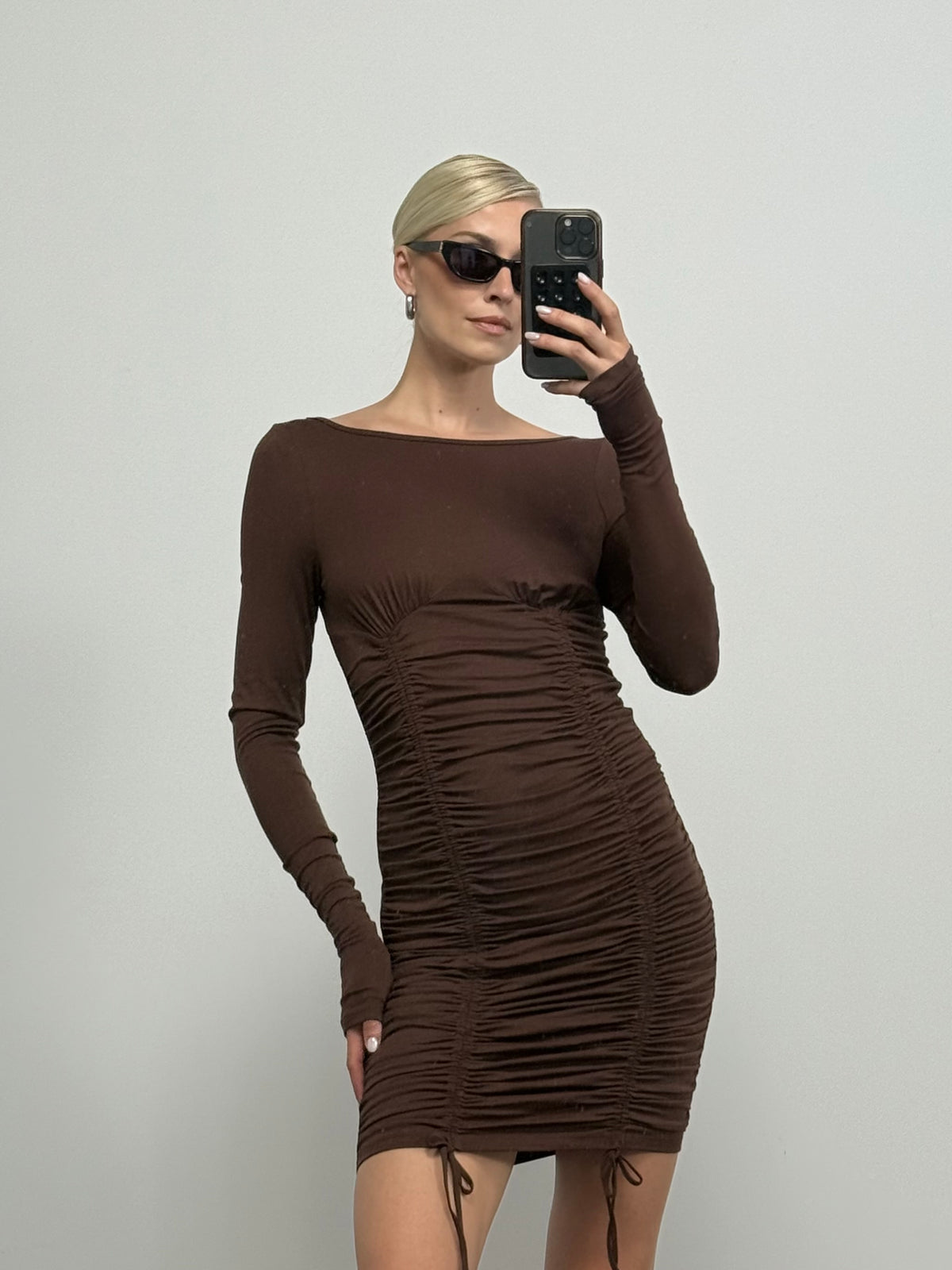 Eine Person, die das Kleid „Kiki“ von LeGer by Lena Gercke und eine Sonnenbrille trägt und vor einer schlichten weißen Wand ein Spiegel-Selfie macht.