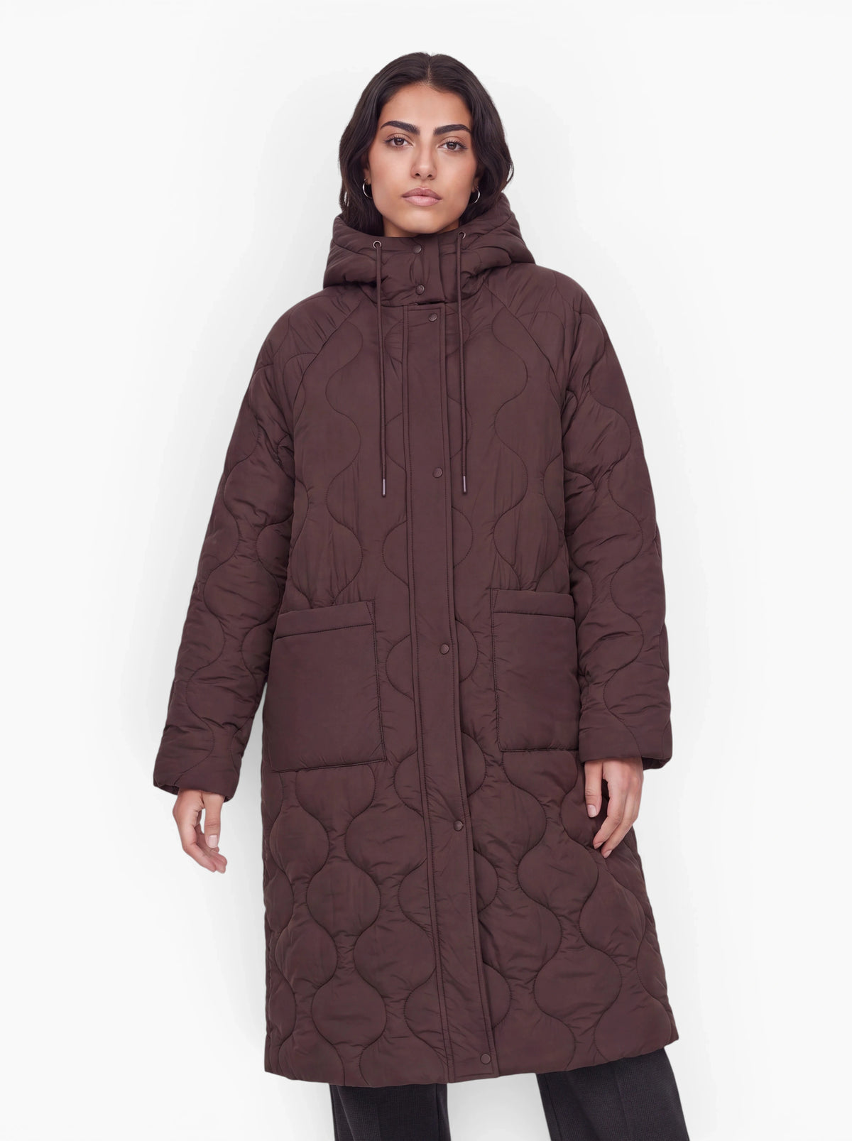 Eine Person trägt den langen, dunkelbraunen „Fray“-Mantel von LeGer by Lena Gercke, der sich durch einen Oversize-Schnitt, Vordertaschen und eine Kapuze auszeichnet, und steht vor einem schlichten weißen Hintergrund.