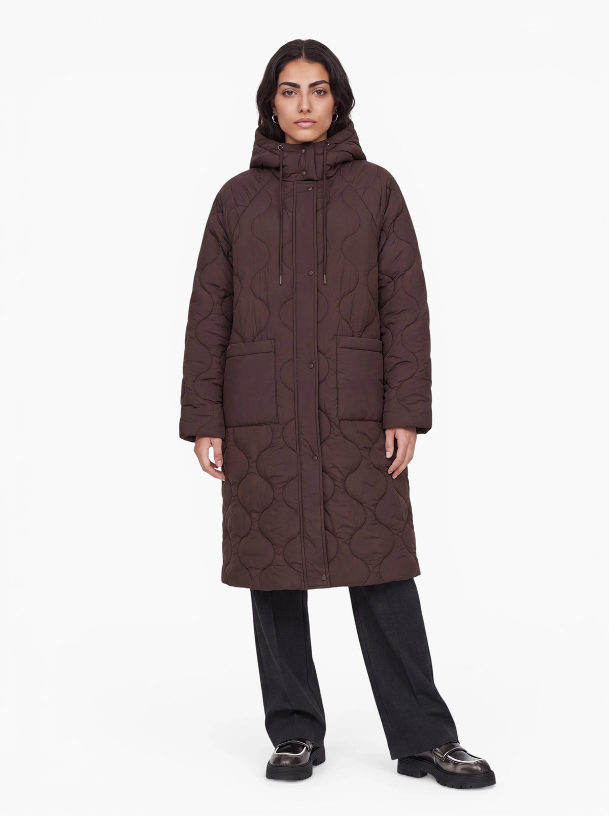 Eine Person steht mit dem Gesicht nach vorne und trägt den langen, dunkelbraunen „Fray“-Mantel von LeGer by Lena Gercke in Oversize-Passform mit Kapuze, dazu schwarze Hosen und schwarze Schuhe vor einem schlichten weißen Hintergrund.