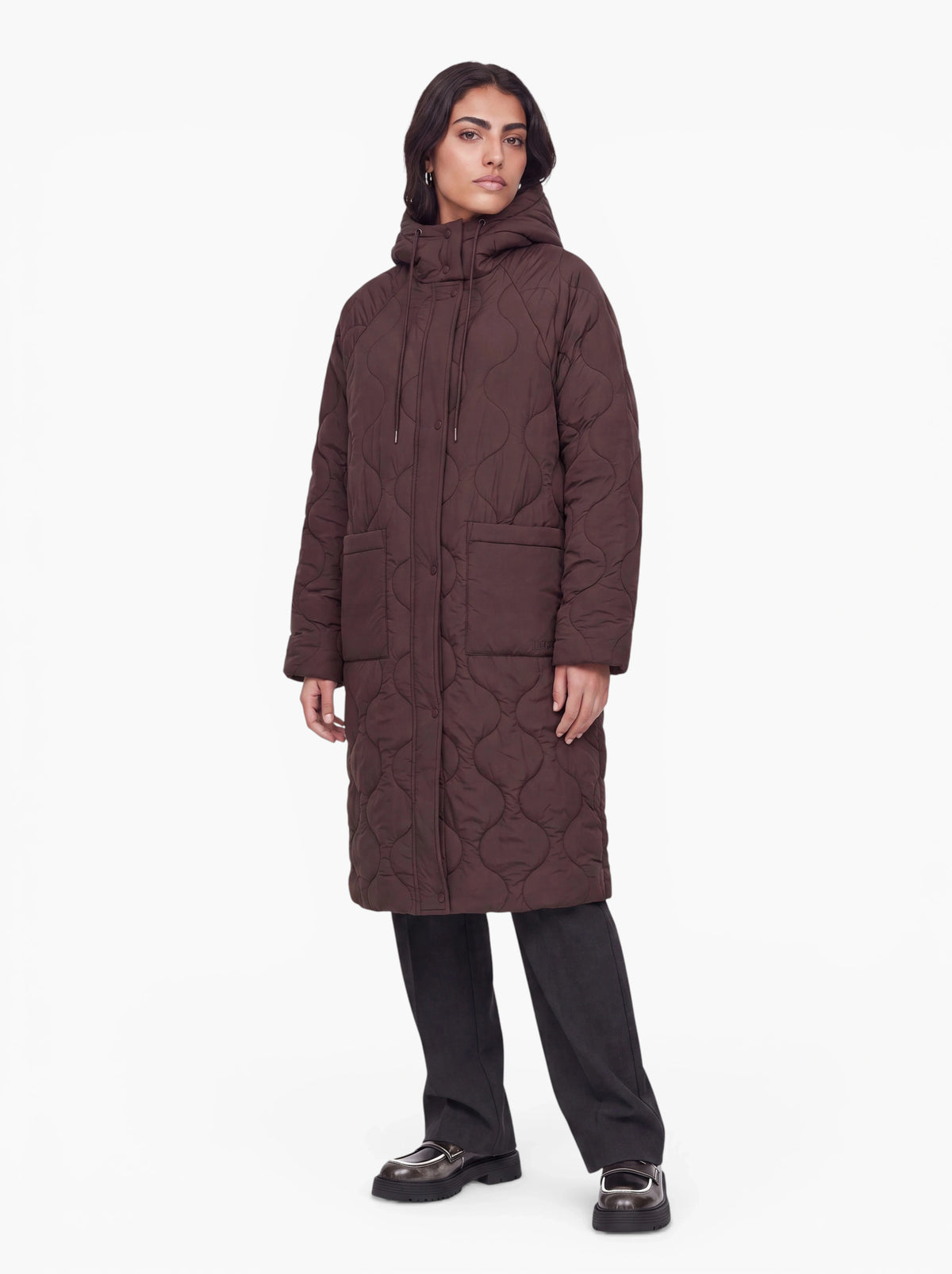 Eine Person, die den langen, dunkelbraunen „Fray“-Mantel von LeGer by Lena Gercke mit Kapuze, einer schwarzen Hose und schwarzen Schuhen trägt, steht mit dem Gesicht nach vorne vor einem schlichten weißen Hintergrund.
