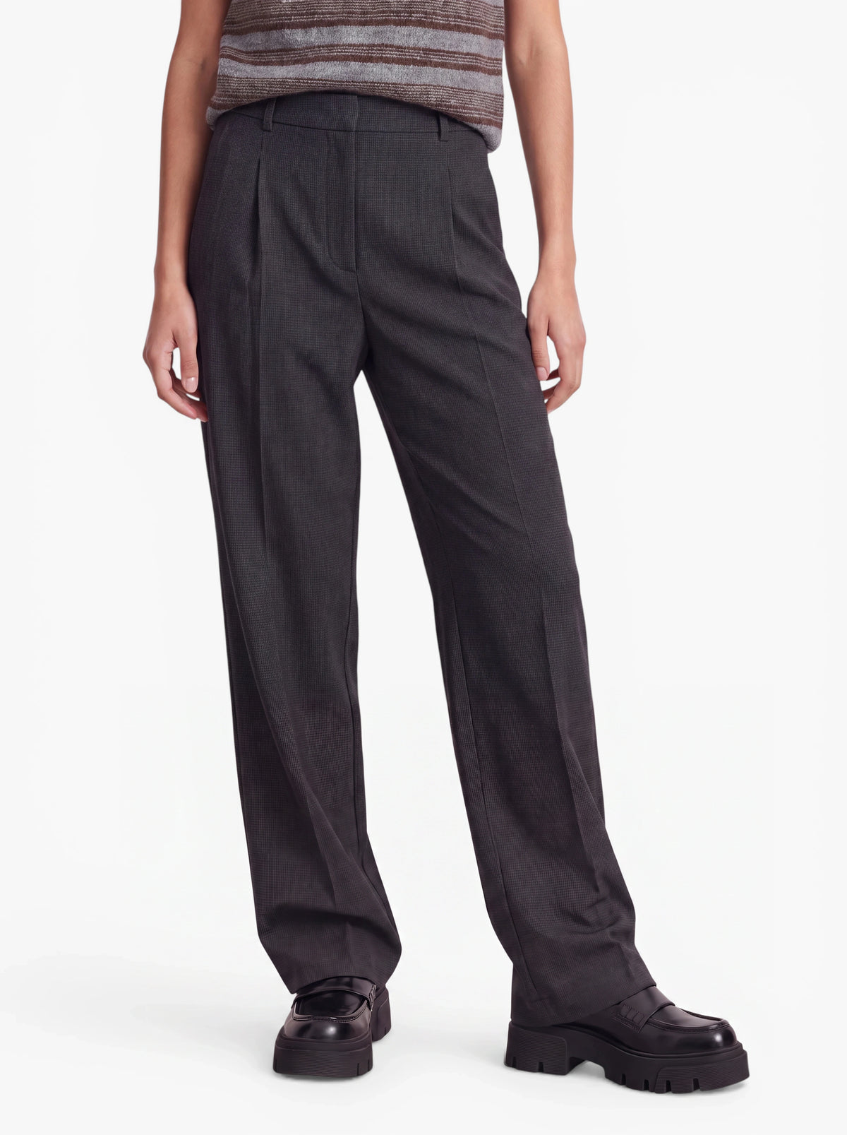 Eine Person trägt eine dunkelgraue „Julie“-Hose mit hoher Taille von LeGer by Lena Gercke sowie schwarze, klobige Schuhe und steht vor einem schlichten weißen Hintergrund. Der Oberkörper ist teilweise zu sehen, die Hände hängen entspannt an den Seiten.