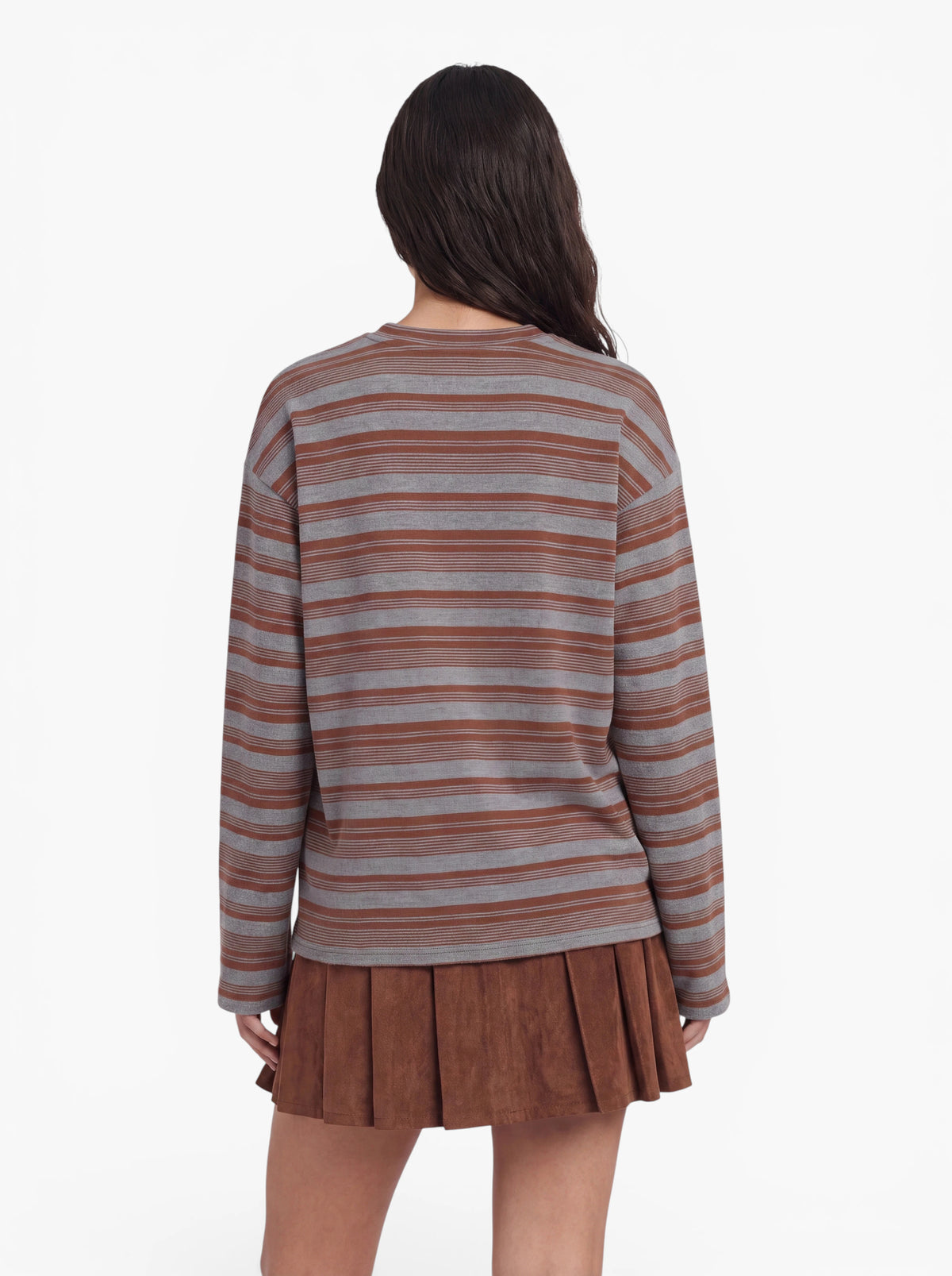 Eine Person mit langen dunklen Haaren, die das Langarmshirt „Vivian“ von LeGer by Lena Gercke in grau-braunen Streifen und einen braunen Faltenrock trägt, steht mit dem Rücken zur Kamera vor einem weißen Hintergrund.