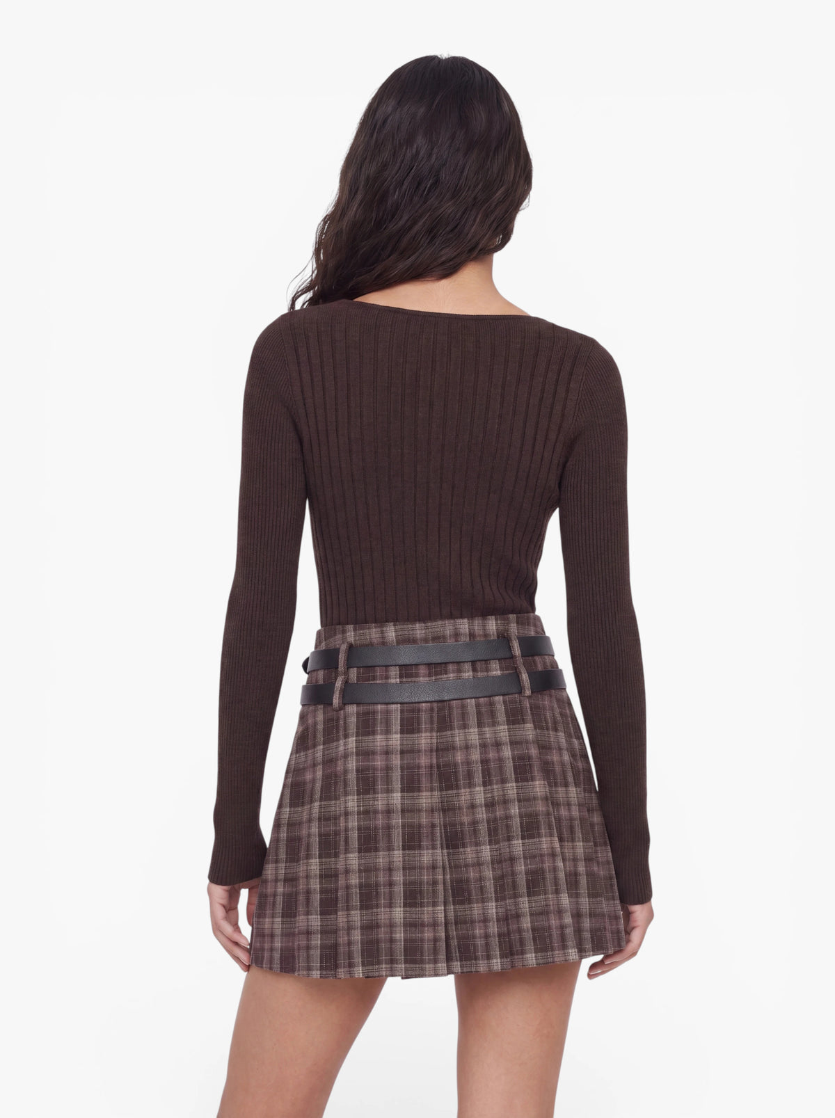 Eine Frau mit langen, gewellten Haaren steht mit dem Rücken zur Kamera vor einem weißen Hintergrund und trägt den Pullover „Selina“ von LeGer by Lena Gercke – einen olivgrünen, gerippten Strickpullover mit asymmetrischem Ausschnitt –, kombiniert mit einem braunen Karorock mit schwarzen Gürteldetails.