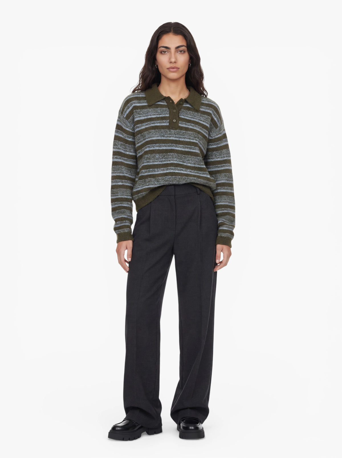 Eine Person steht mit dem Gesicht nach vorne und trägt den Pullover „Delia“ von LeGer by Lena Gercke mit olivgrünen Streifen und einem Hemdkragen, dazu eine dunkle Hose mit weitem Bein. Sie hat langes dunkles Haar und trägt schwarze Schuhe und posiert vor einem schlichten weißen Hintergrund.
