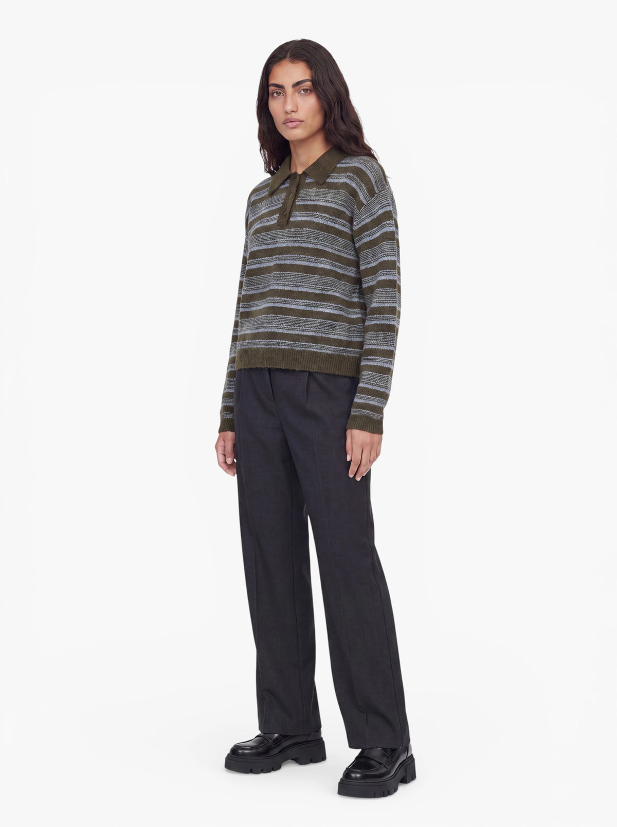 Eine Person, die den Pullover „Delia“ von LeGer by Lena Gercke mit Hemdkragen und olivgrünen Streifen trägt, kombiniert mit einer dunklen Hose mit weitem Bein und schwarzen Plateauschuhen, steht mit dem Blick nach vorne vor einem schlichten weißen Hintergrund.